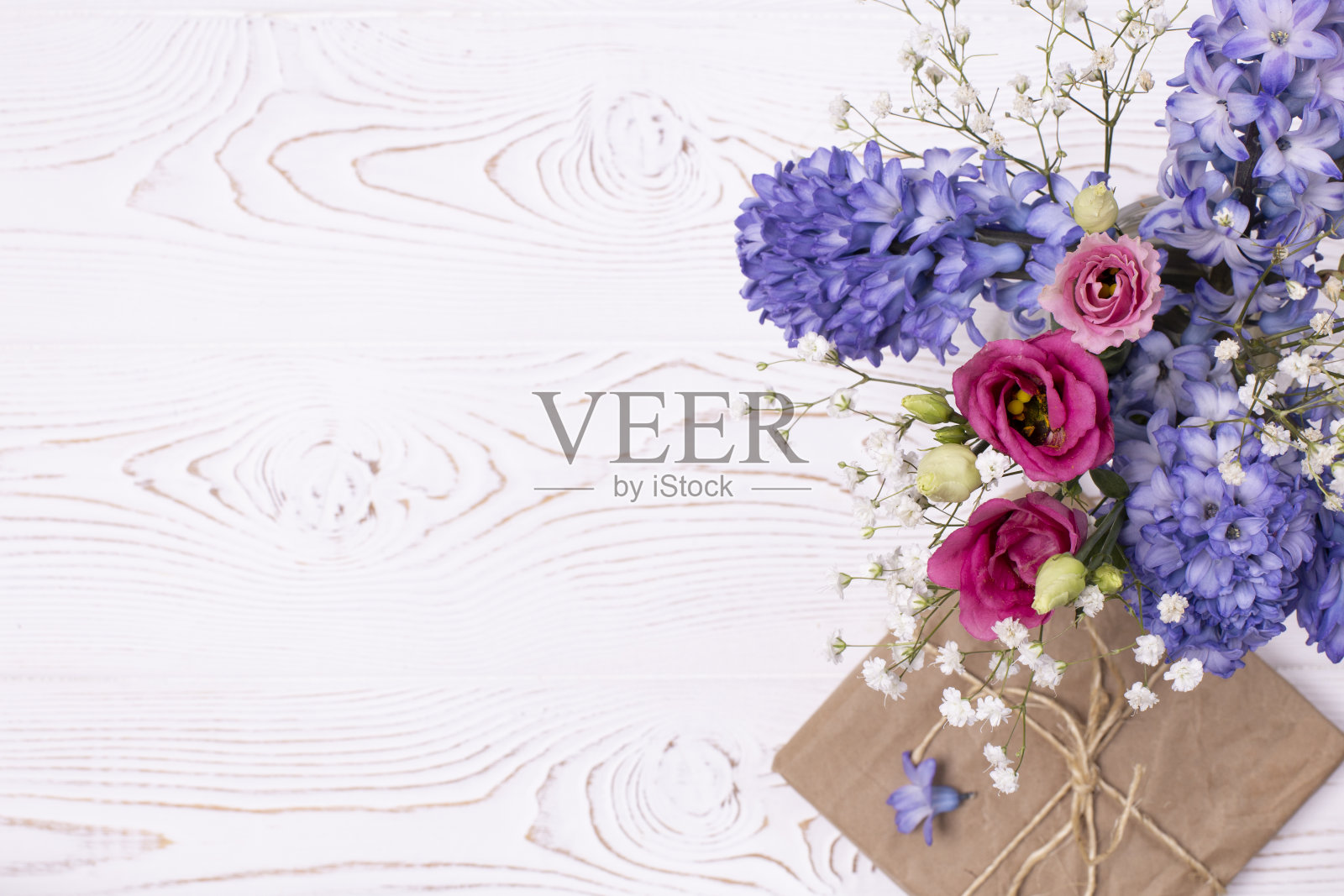 一个用牛皮纸包着的礼盒，白色的桌面上放着蓝色的风信子花和粉色的玫瑰。平的。文本复制空间照片摄影图片
