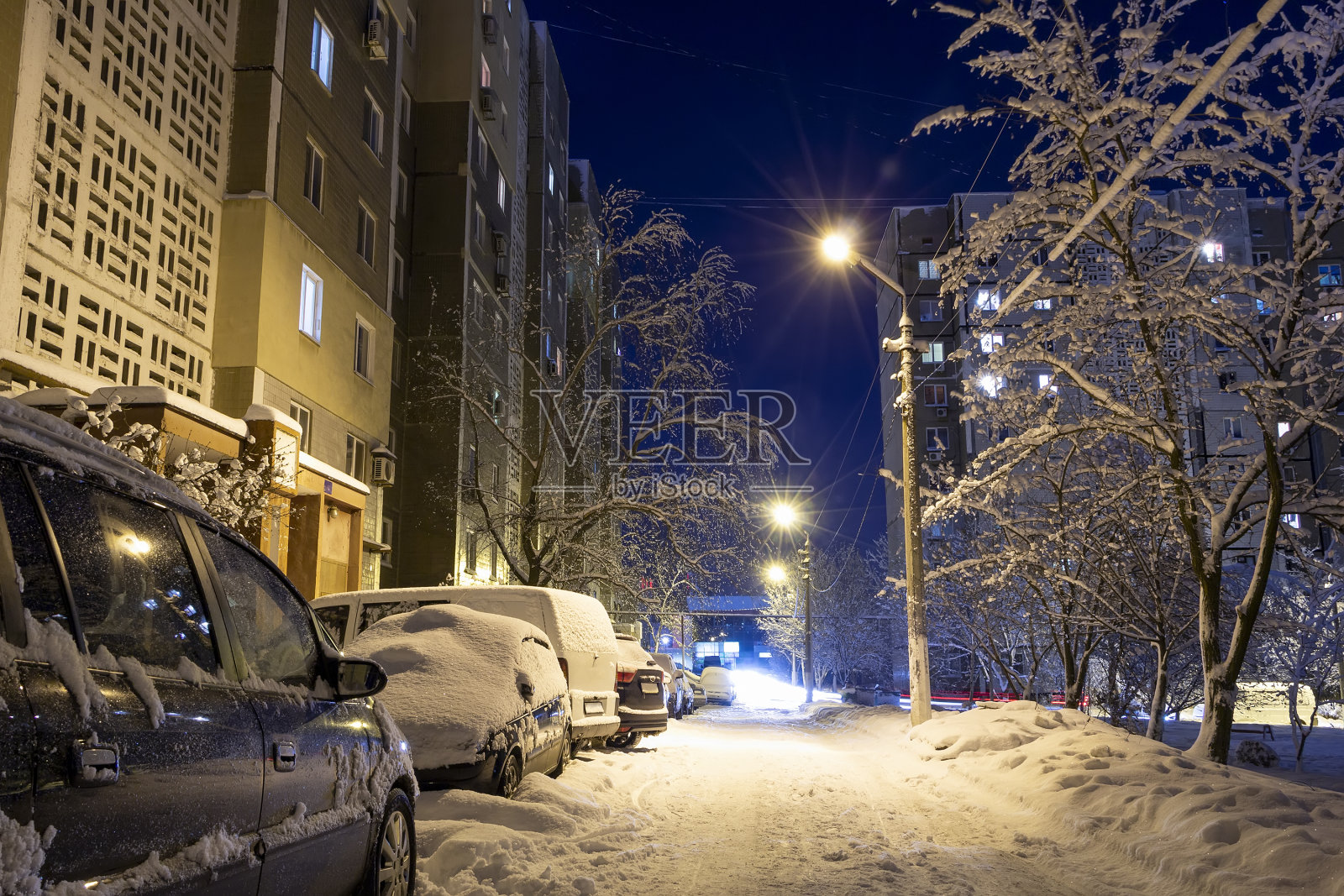 白雪覆盖的城市庭院在深夜。神奇的景观。白雪覆盖的汽车停在高楼大厦旁，灯火通明。乌克兰顿涅茨克的wintertale。从路上看风景照片摄影图片