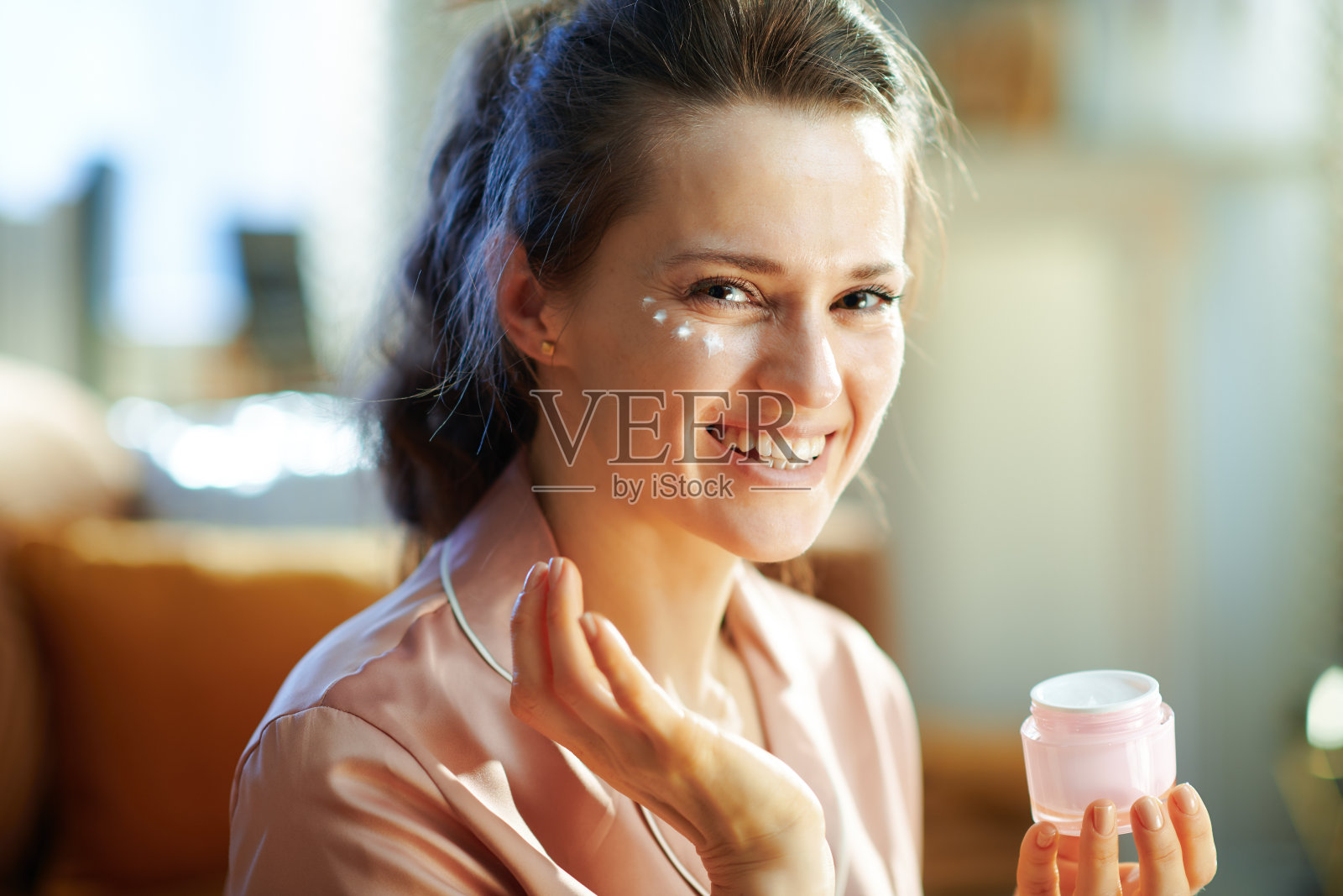 微笑的女人与化妆品罐应用眼霜照片摄影图片