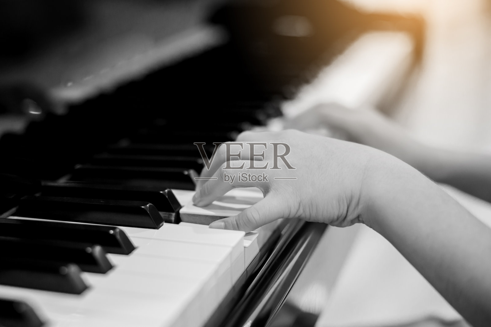 黑白图像。选择性的集中于孩子的手指和钢琴键来弹奏钢琴。有音乐会或学习音乐的乐器。儿童音乐家在舞台上弹奏钢琴的特写手照片摄影图片