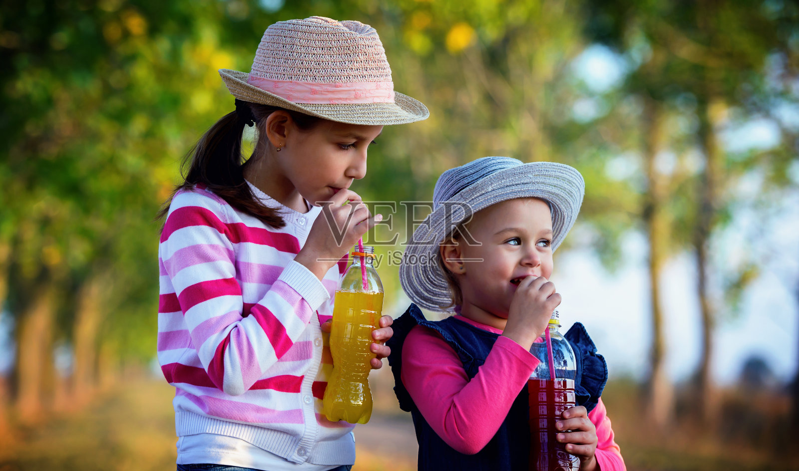 童年时间。两个小女孩在公园里喝果汁照片摄影图片