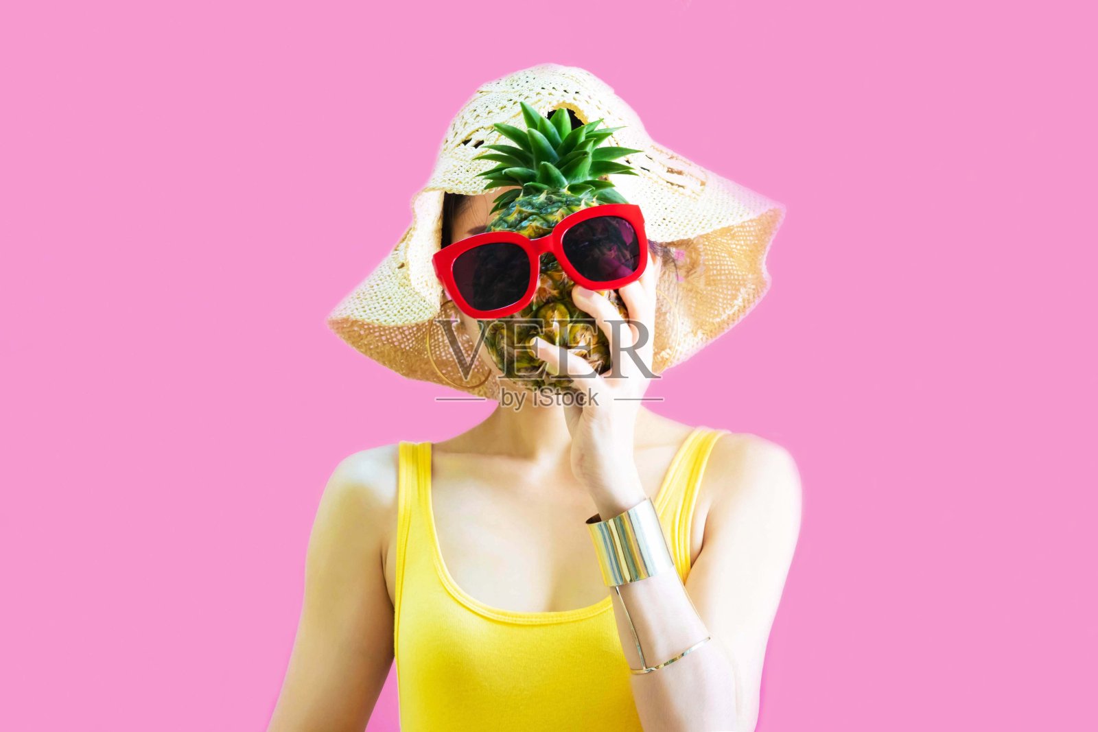 快乐美丽的亚洲女人在黄色汗衫，太阳镜时尚拿菠萝在她的手与菠萝摆pose，女搞笑与菠萝在暑假孤立在粉红色的背景照片摄影图片