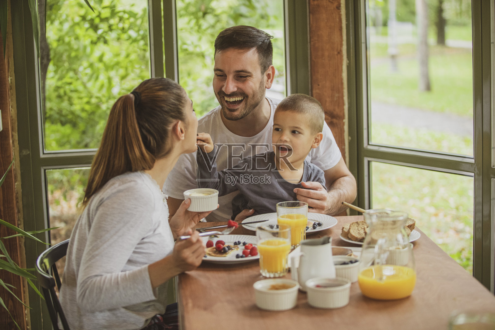 一个年轻的家庭穿着他们的睡衣在一个舒适的小木屋在树林里吃健康的早餐。照片摄影图片