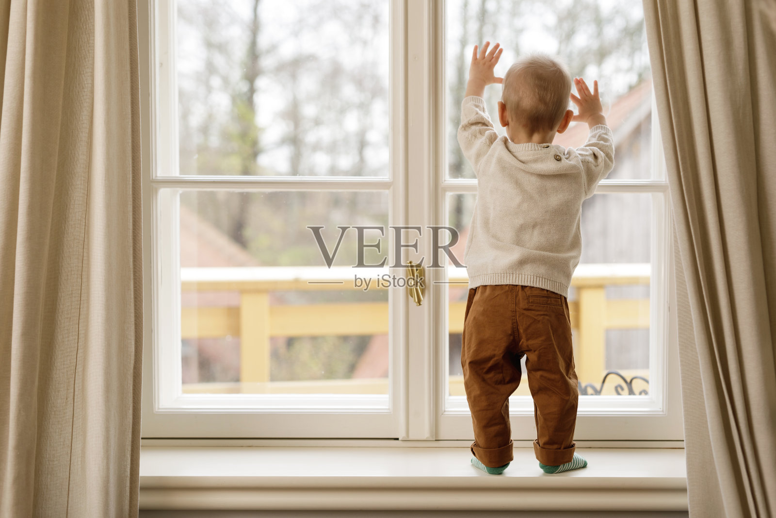 小男孩站在窗台上看窗户照片摄影图片