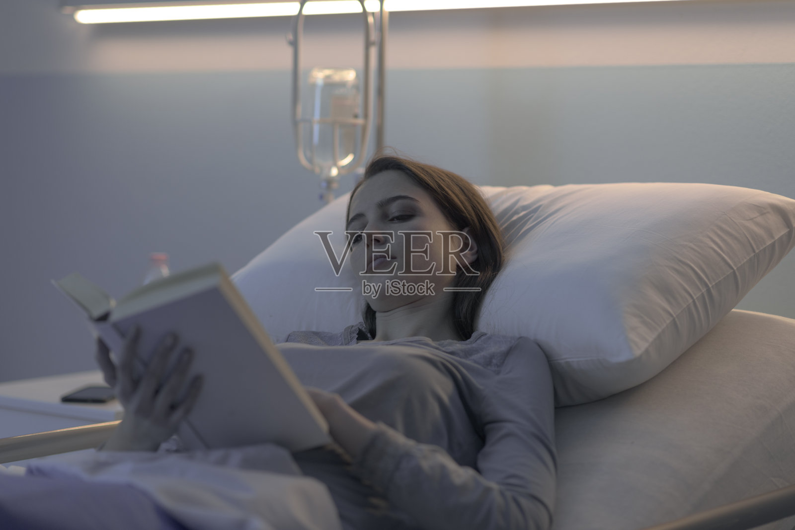 年轻的失眠病人躺在医院的病床上看书照片摄影图片
