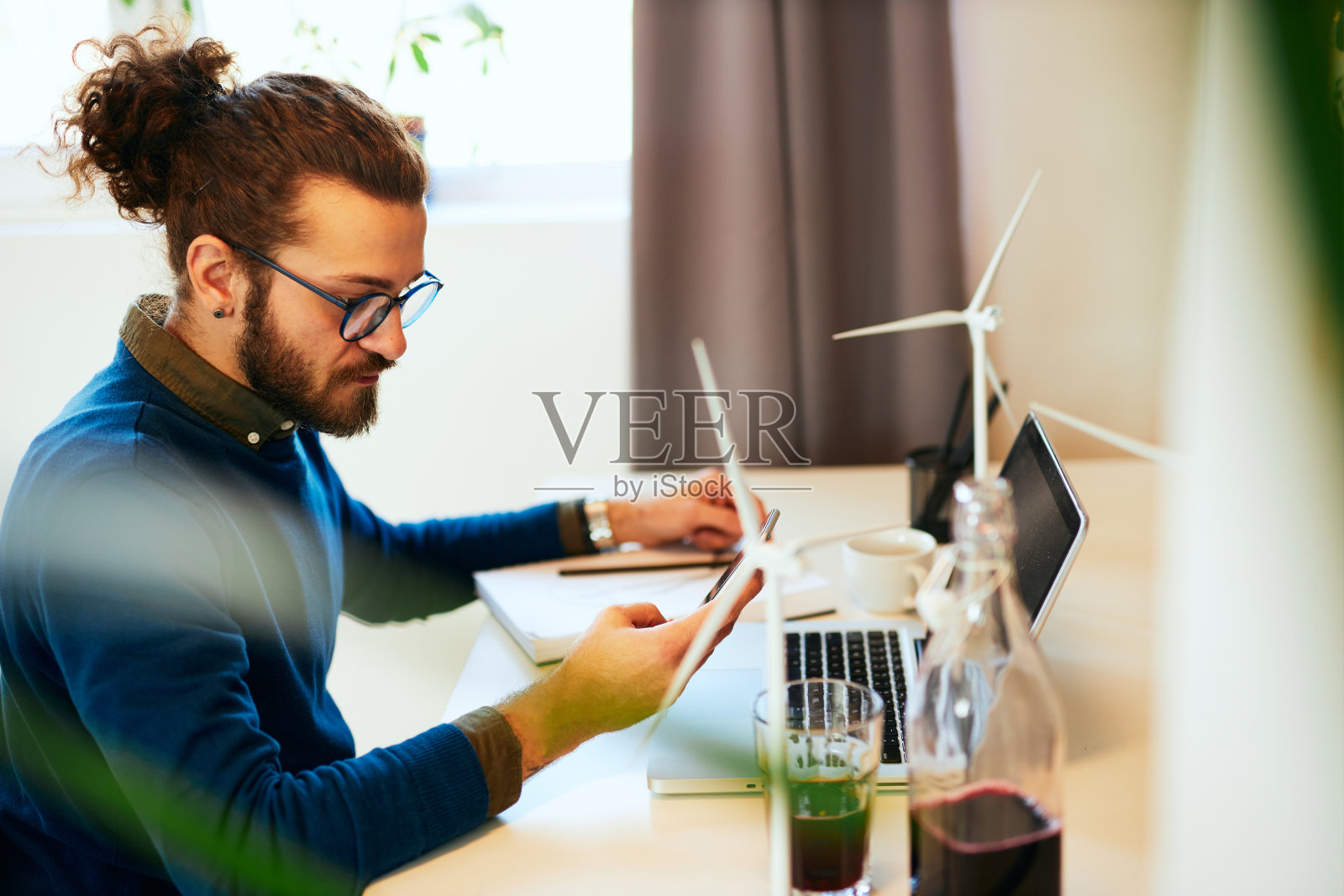 英俊的蓄着胡须的白人企业家坐在他的办公室里，使用智能手机，在工作之余休息一下。照片摄影图片