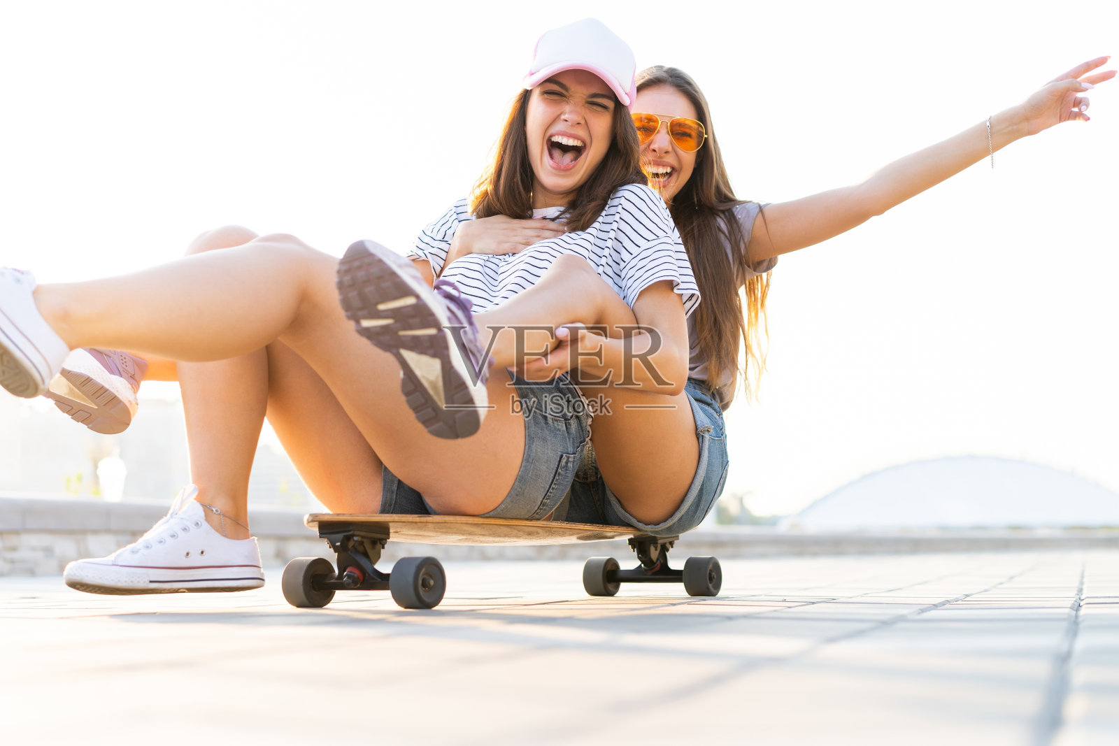 两个微笑的年轻女孩玩滑板在公园。照片摄影图片