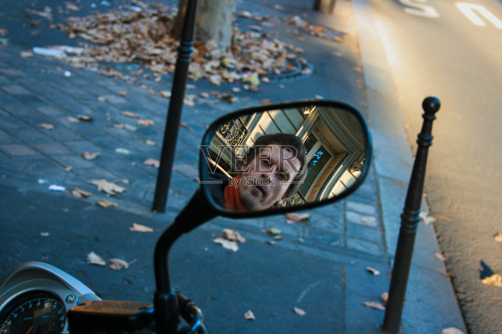 在秋天的街道上，一辆摩托车或摩托车的后视镜映出了一个年轻人的脸。照片摄影图片