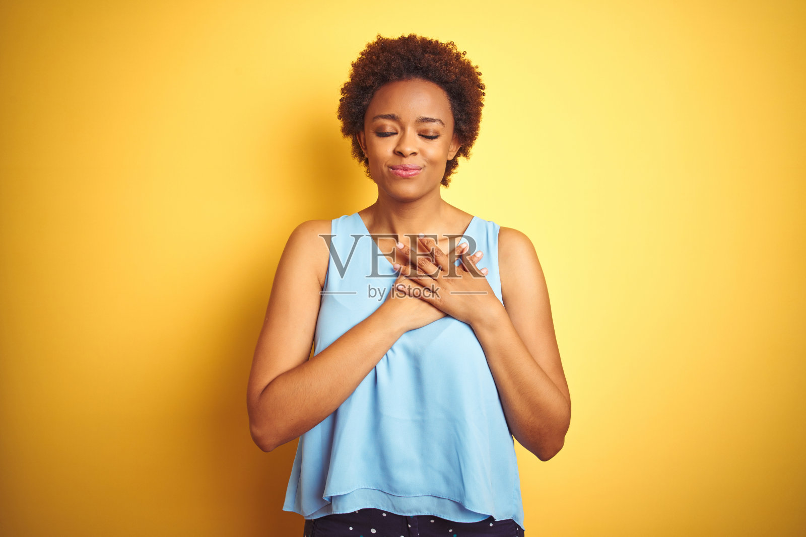 美丽的非洲裔美国女人穿着优雅的衬衫在孤立的黄色背景微笑与手在胸前闭上眼睛和感激的手势在脸上。健康的概念。照片摄影图片