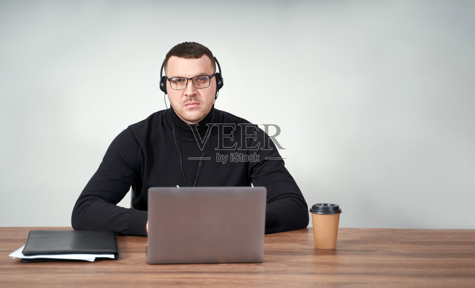注意力集中的人戴着耳机使用笔记本电脑，而坐在灰色背景与背景照片摄影图片
