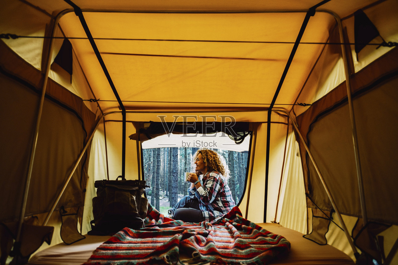 快乐孤独的成年白人妇女坐在帐篷外享受一杯茶和野外自然周围-免费的替代露营度假帐篷和背包的旅游癖的人上瘾照片摄影图片