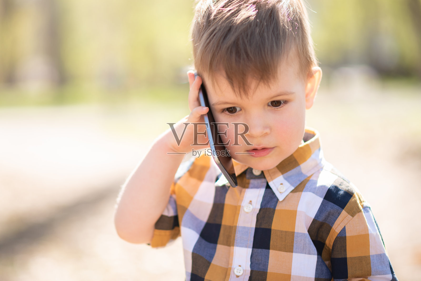 小男孩在公园里用智能手机说话照片摄影图片