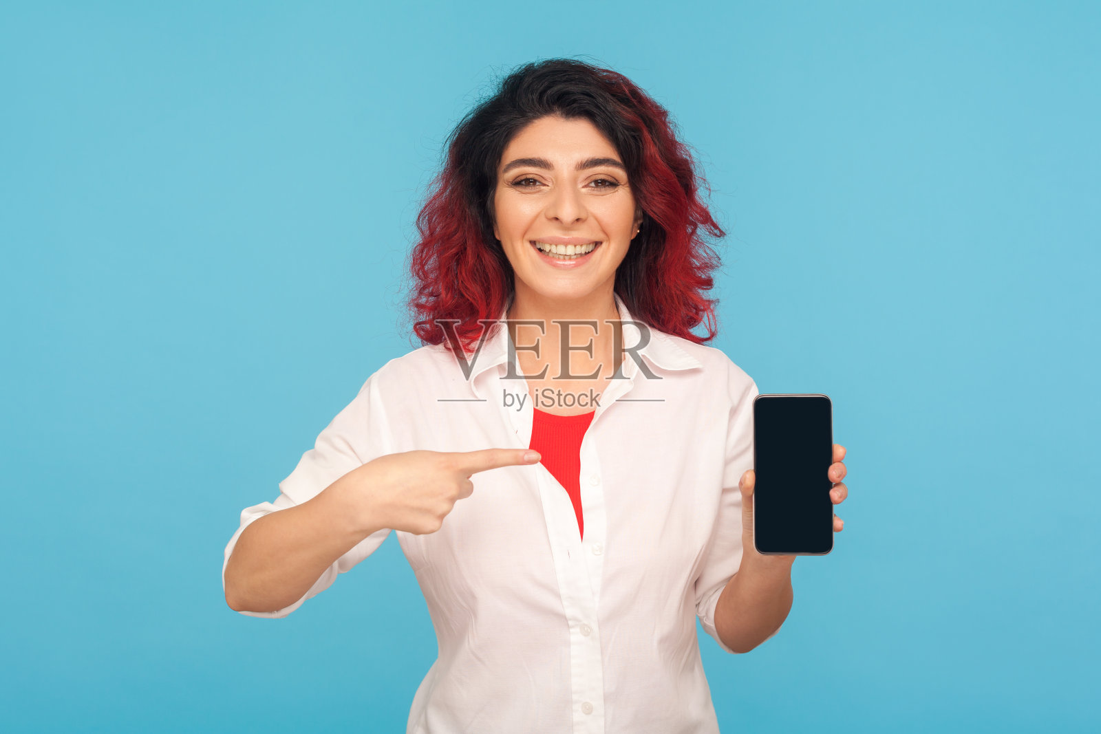 一幅快乐漂亮的时髦女人的肖像，她有着漂亮的红头发，指着智能手机微笑着照片摄影图片