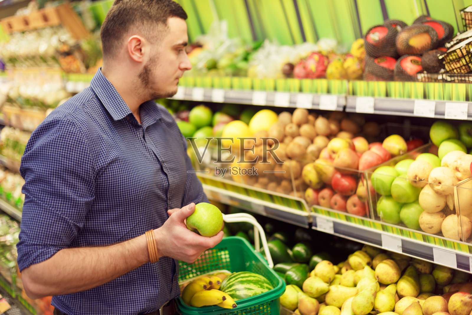 男子在超市的货架上为水果购买杂货，他正在检查苹果。照片摄影图片