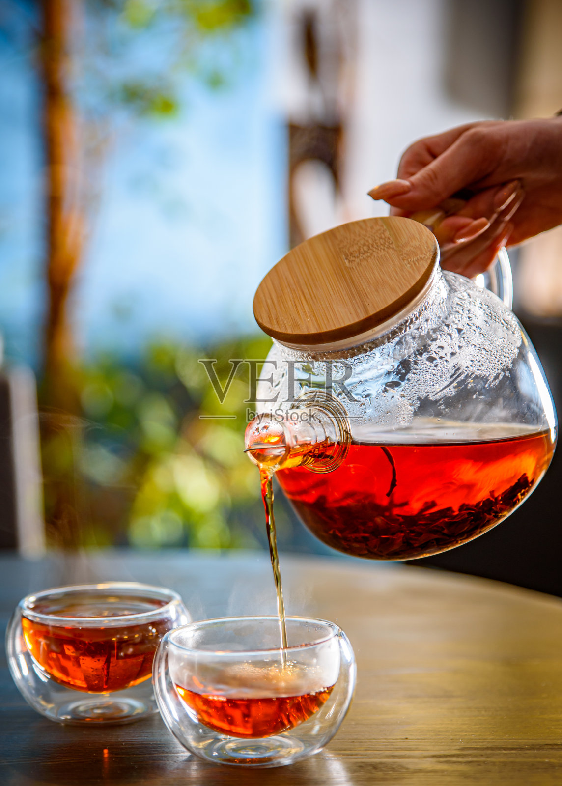 把茶从玻璃茶壶倒进咖啡馆桌上的杯子里照片摄影图片