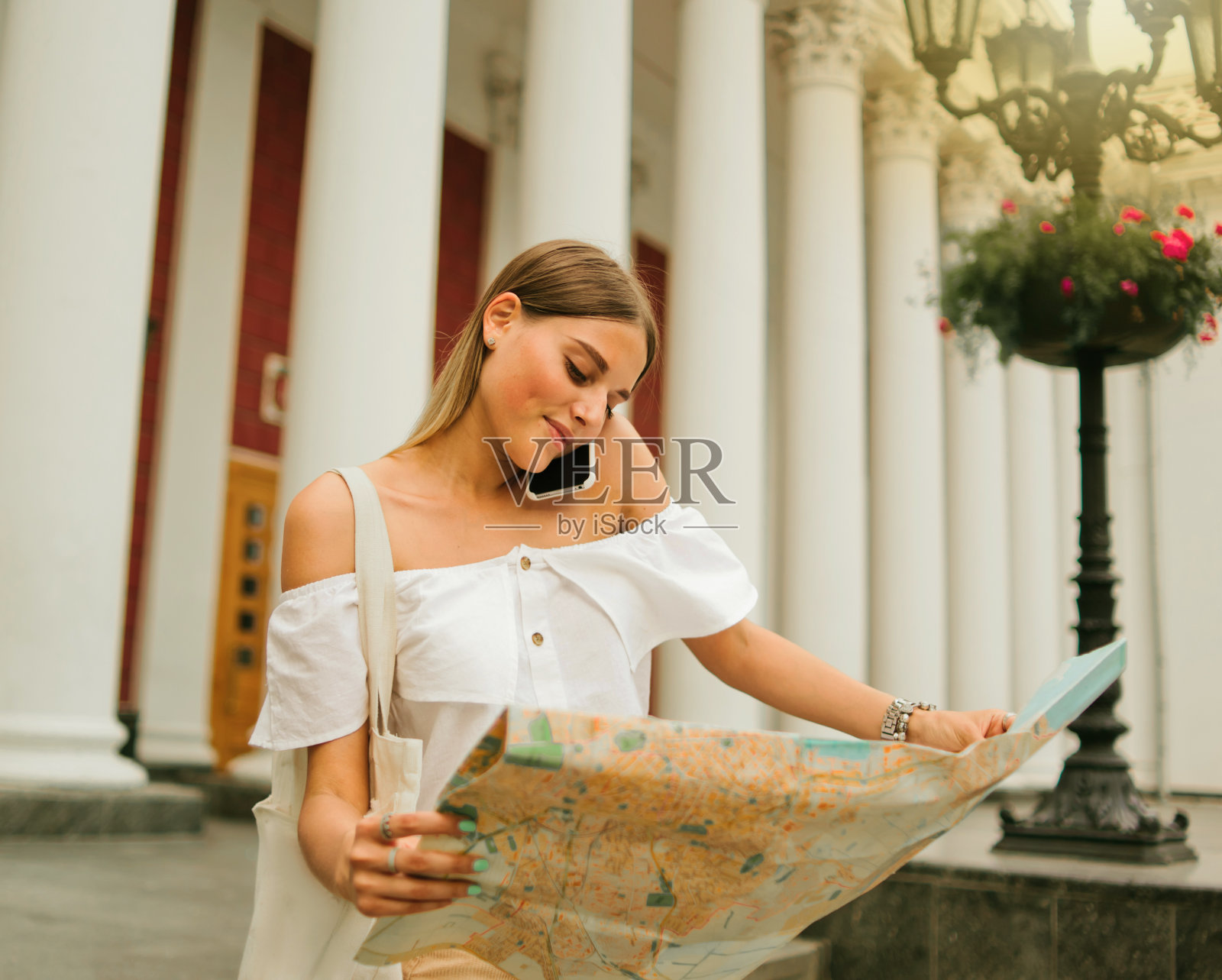 年轻的美女游客探索城市地图和谈论在城市环境的柱子背景下的电话照片摄影图片