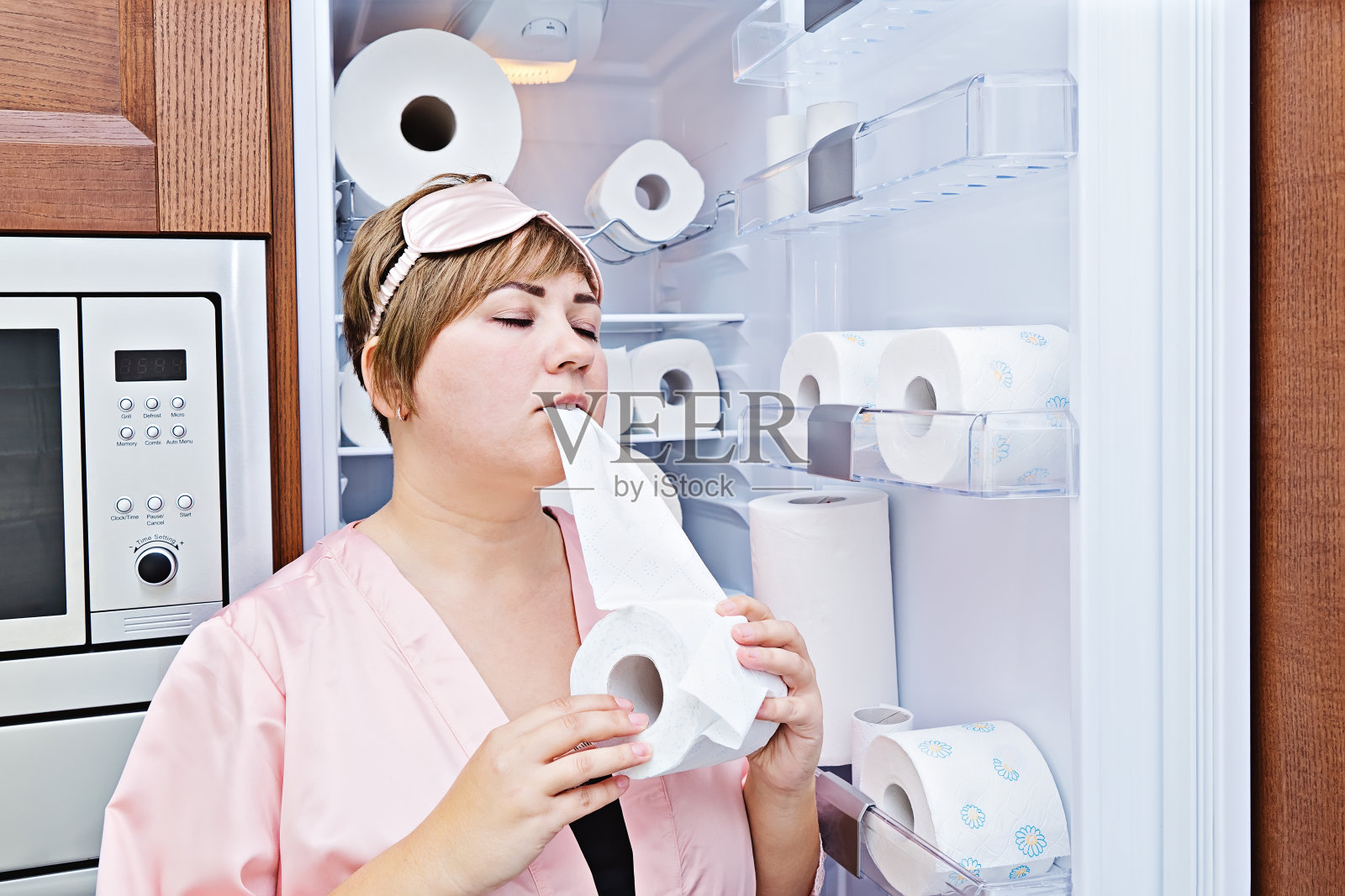 一个穿着睡衣的女人在装满厕纸的冰箱旁边贪婪地吃厕纸照片摄影图片