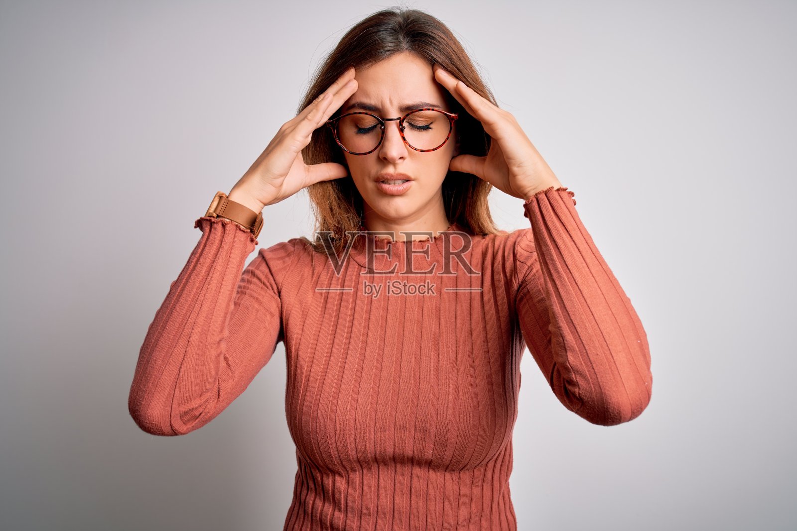 年轻美丽的黑发女人穿着休闲毛衣和眼镜在白色的背景与手在头上疼痛，因为压力。遭受偏头痛。照片摄影图片