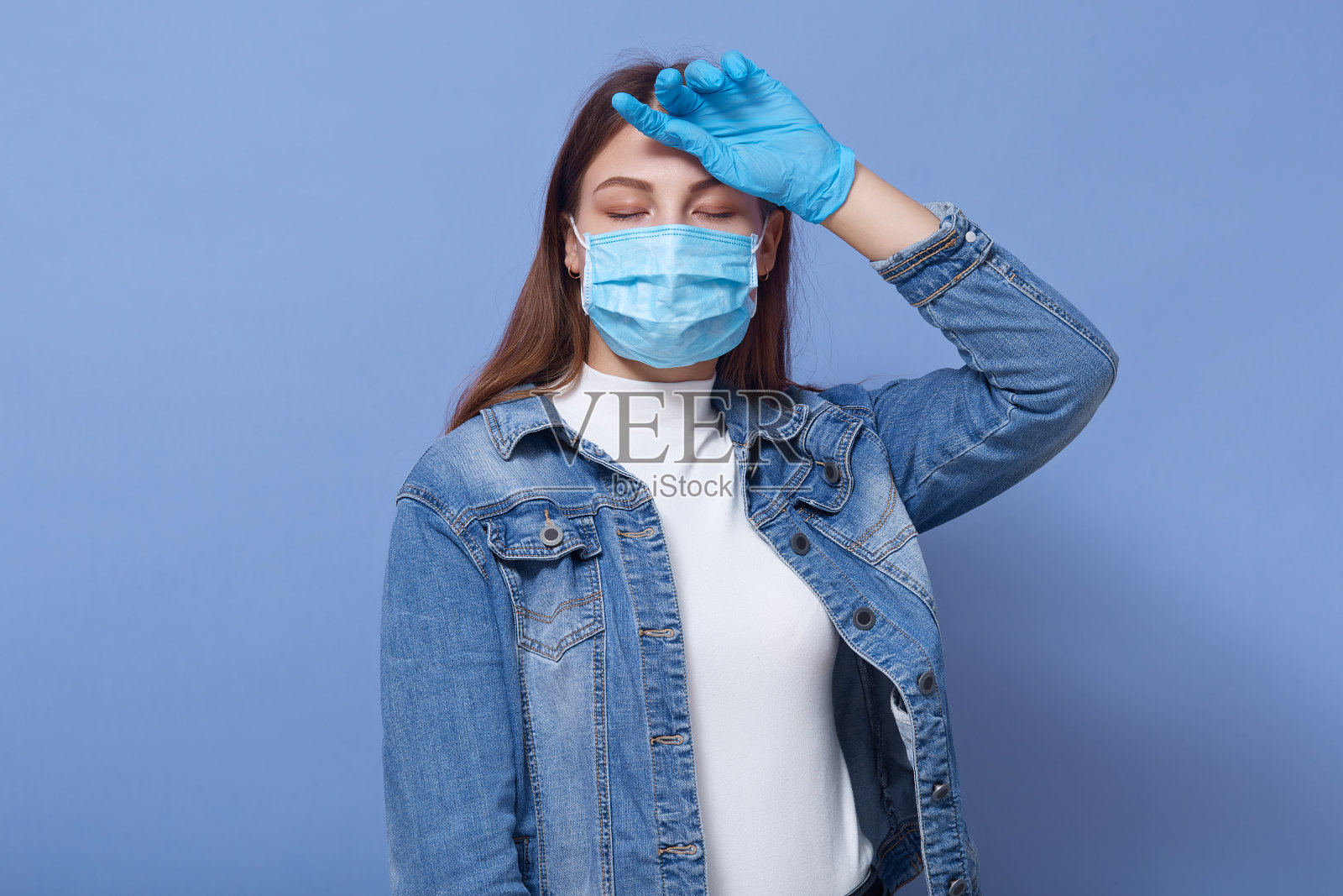 疲惫的患病年轻女性发烧，一只手放在额头，感觉不适，闭上双眼，患新冠肺炎，戴抗菌口罩和手套。冠状病毒的概念。照片摄影图片