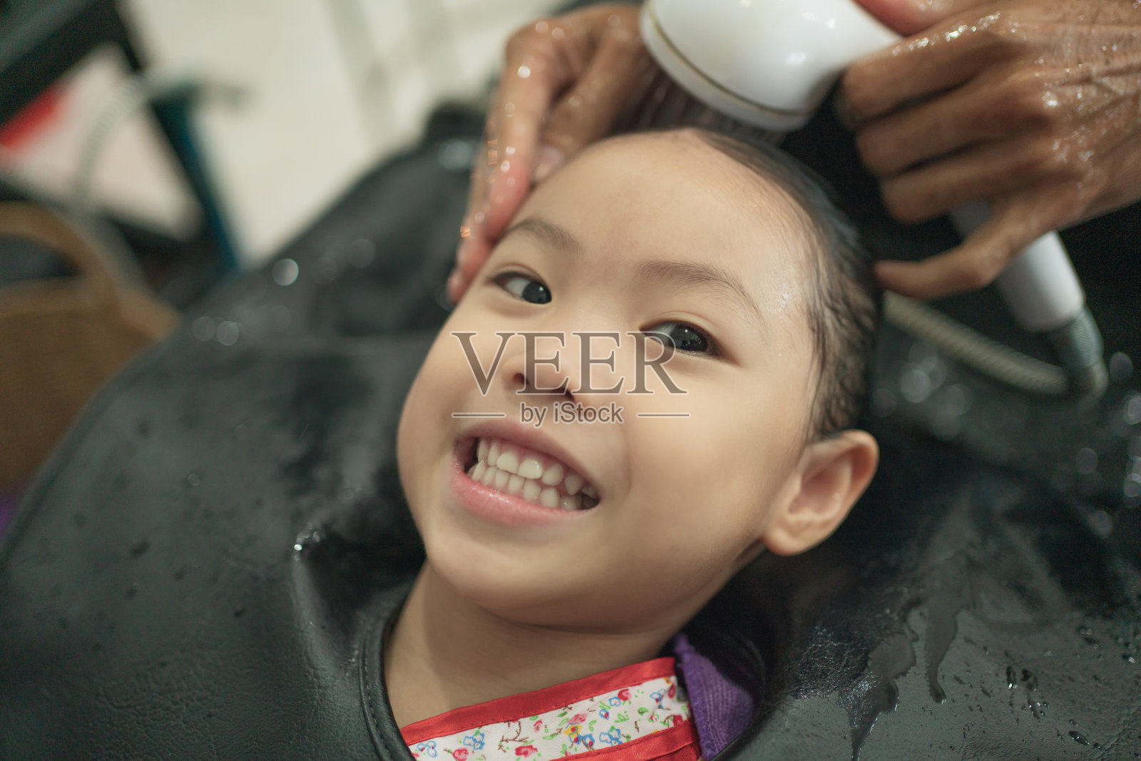 一个亚洲小女孩在美容院洗头。理发师为她的客户洗头。小女孩很快乐，喜欢洗头发。照片摄影图片
