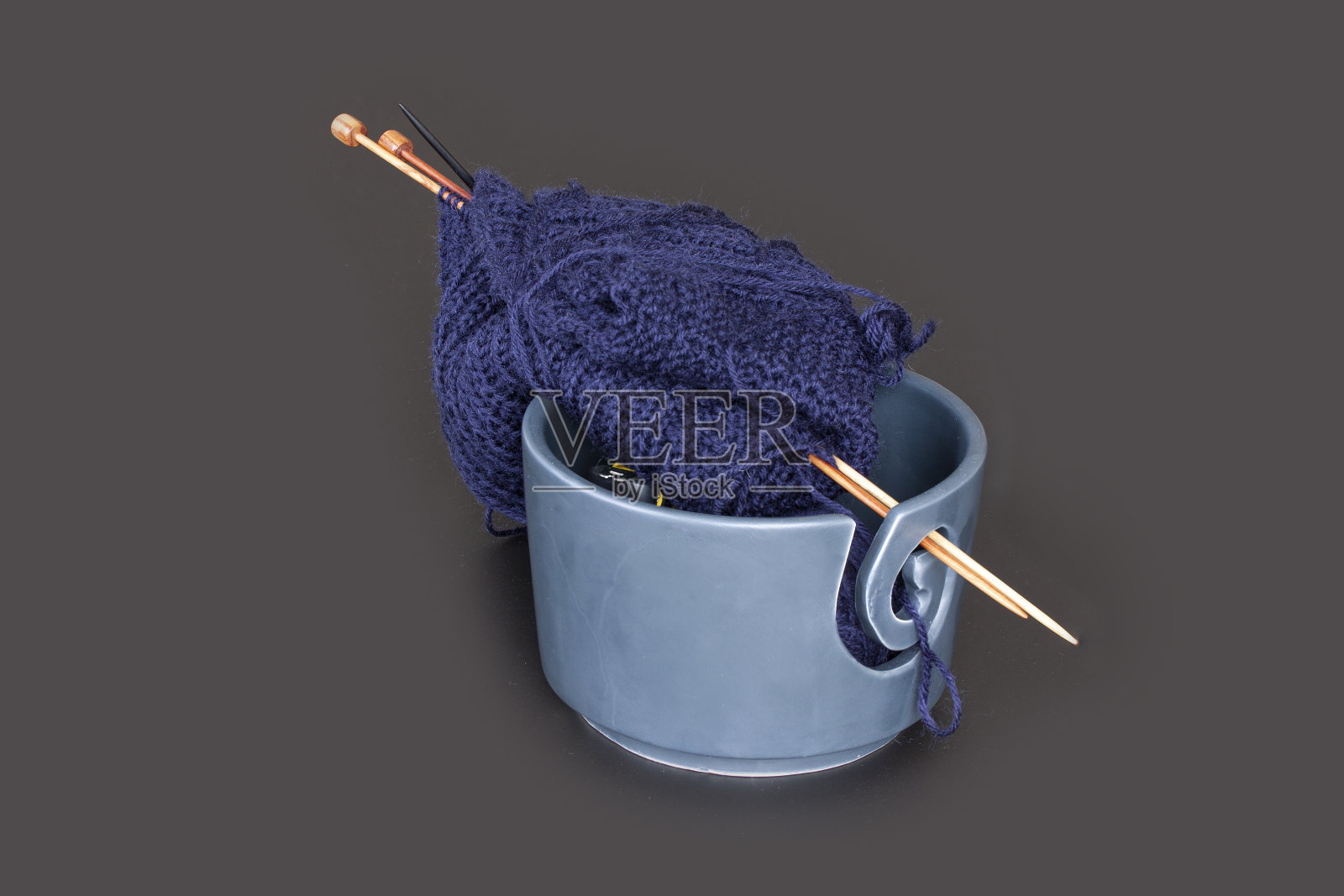 针织工具，用于编织的毛线球和木针。蓝色纱线在碗里孤立在深灰色的背景桌上。有拷贝空间的静物。照片摄影图片