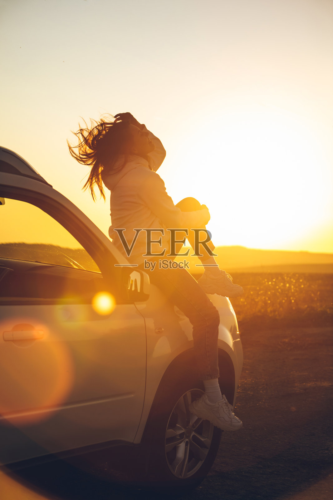 女人停在路边欣赏日落。坐在车盖上照片摄影图片