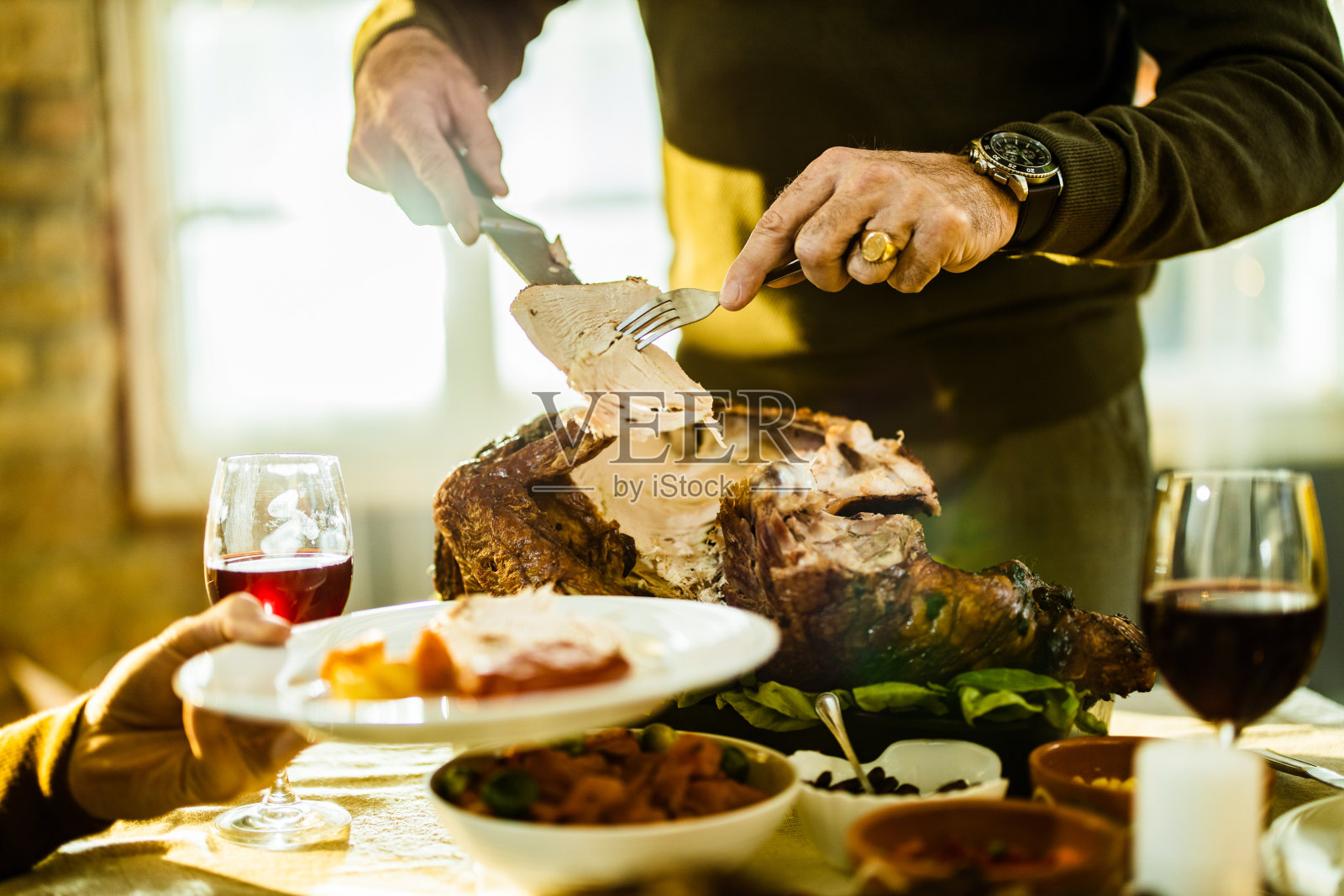 一个面目全非的人正在切火鸡肉，放在家里的盘子里。照片摄影图片
