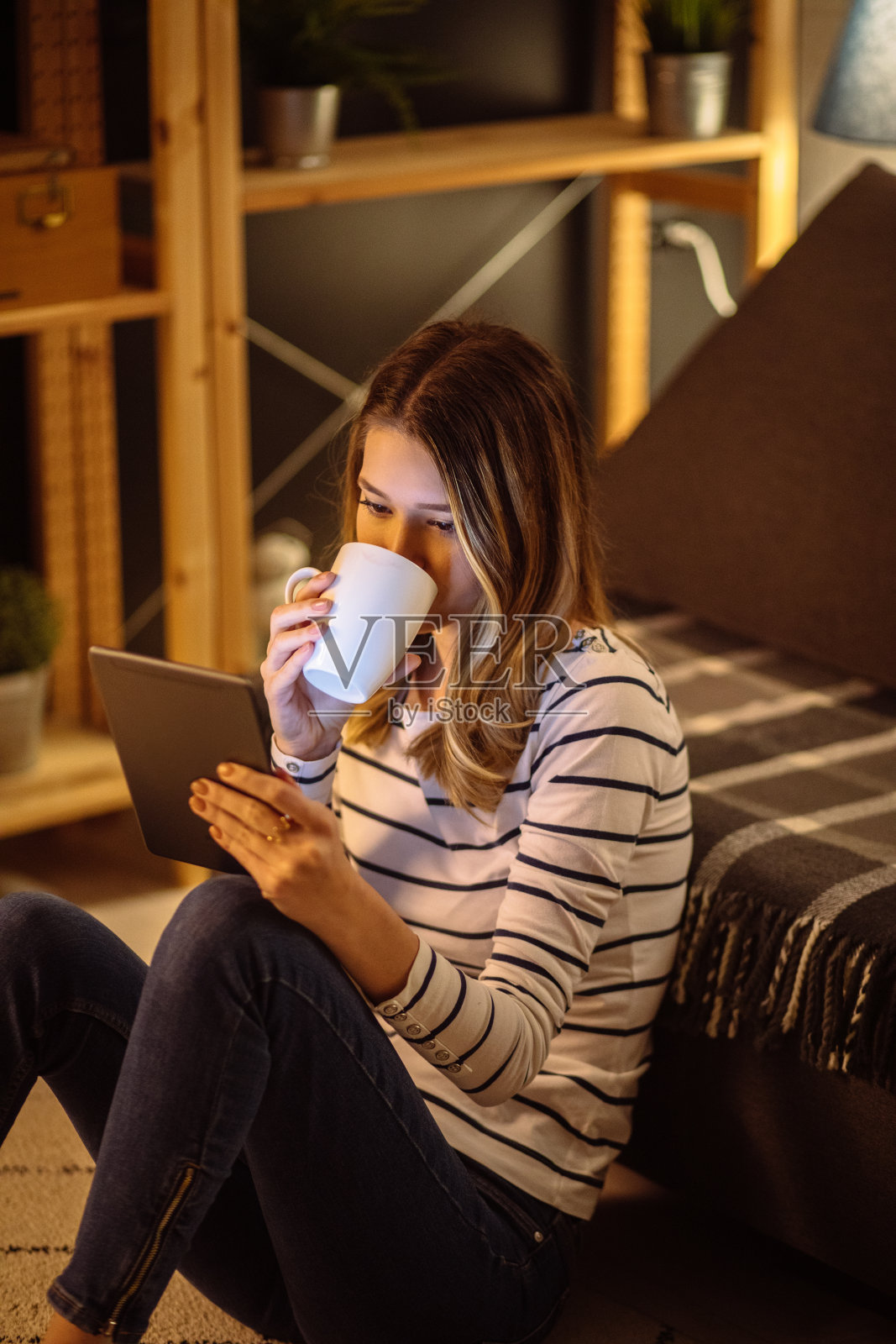年轻女子晚上在客厅里用着平板电脑喝茶照片摄影图片