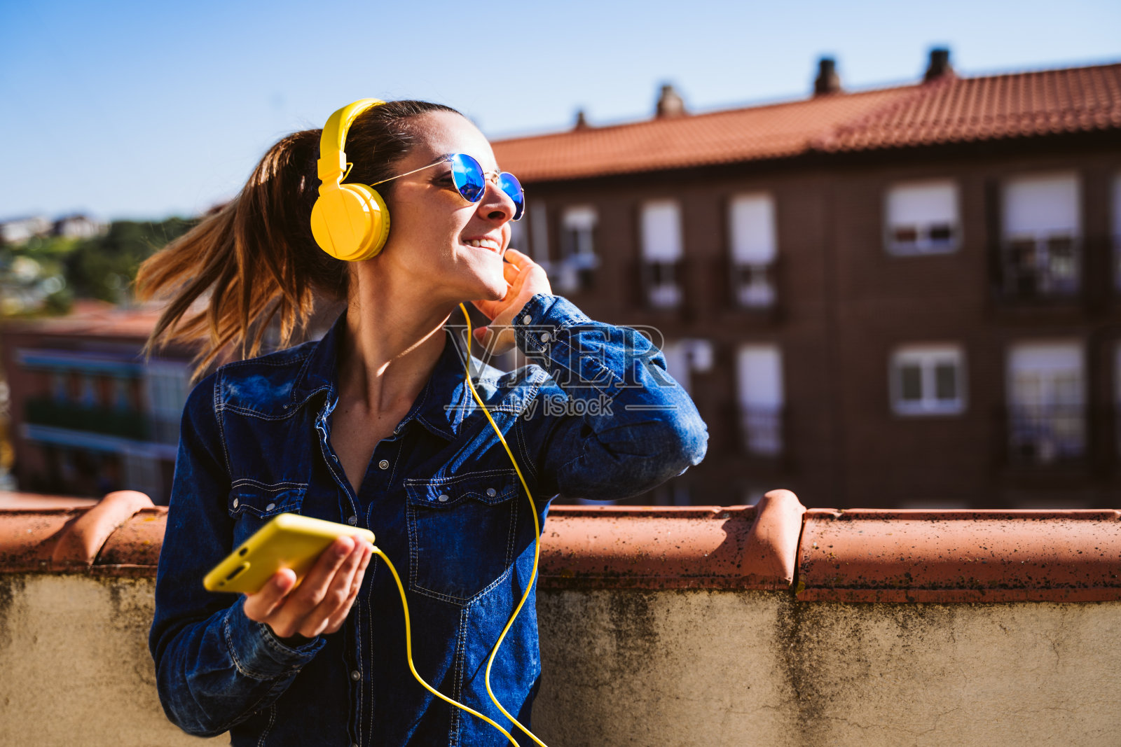 年轻女子正在用手机和黄色耳机听音乐。乐趣和生活方式照片摄影图片