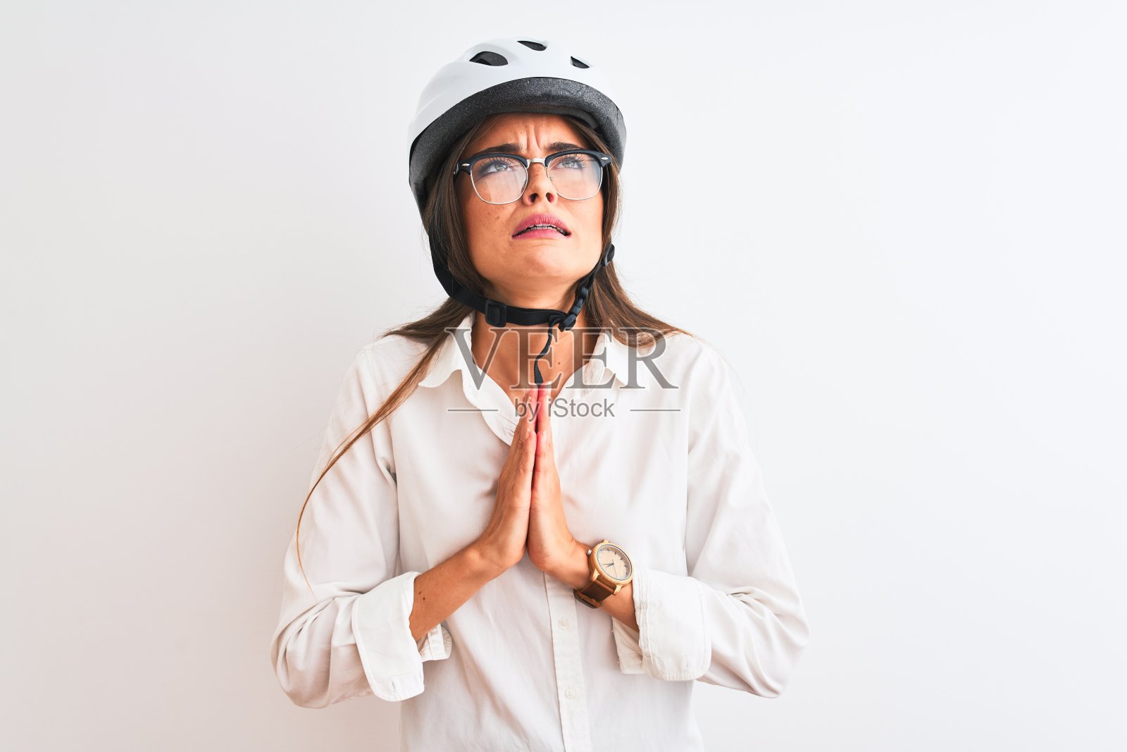 美丽的女商人戴着眼镜和自行车头盔，在孤立的白色背景下乞讨和祈祷，双手在一起，脸上的希望表情非常情绪化和担心。请求宽恕。宗教的概念。照片摄影图片