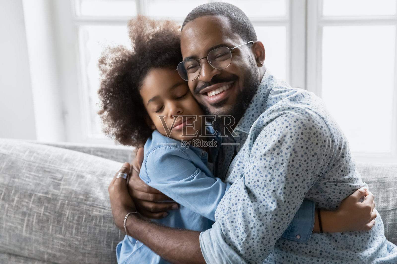 慈爱的非洲父亲坐在沙发上拥抱小女儿照片摄影图片