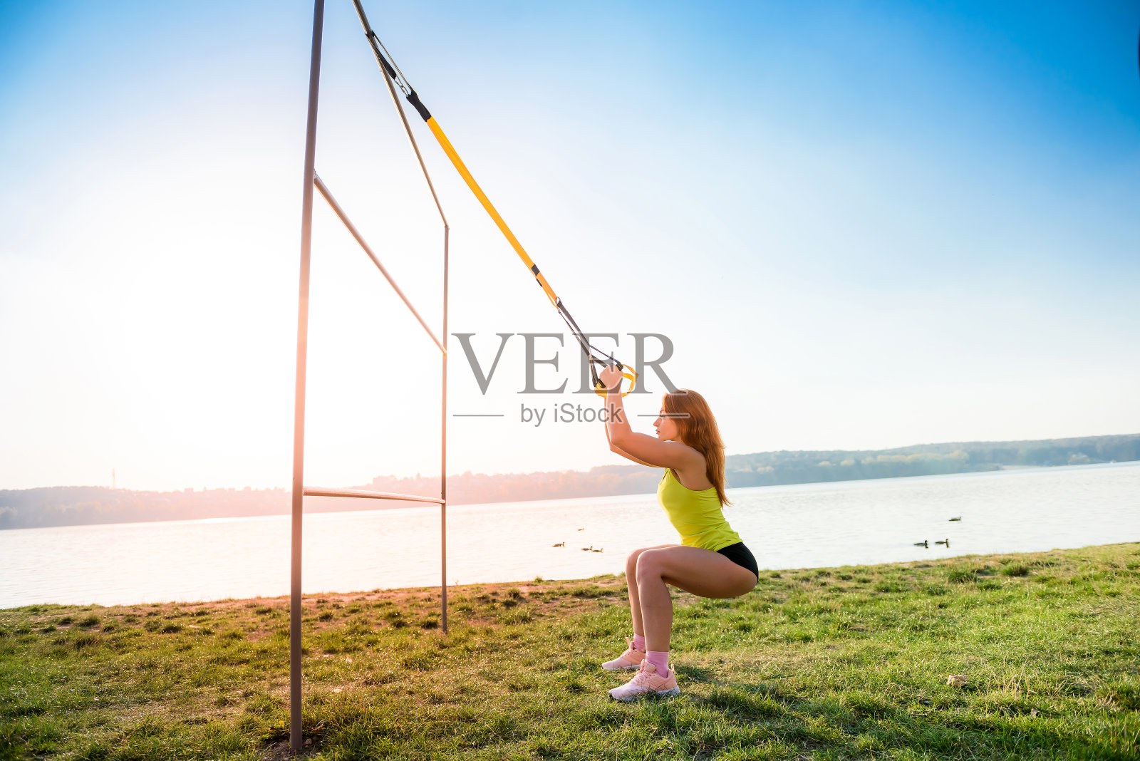 穿着运动服的漂亮女人白天在湖边户外用trx健身带做健身房俯卧撑。健康的生活方式。照片摄影图片