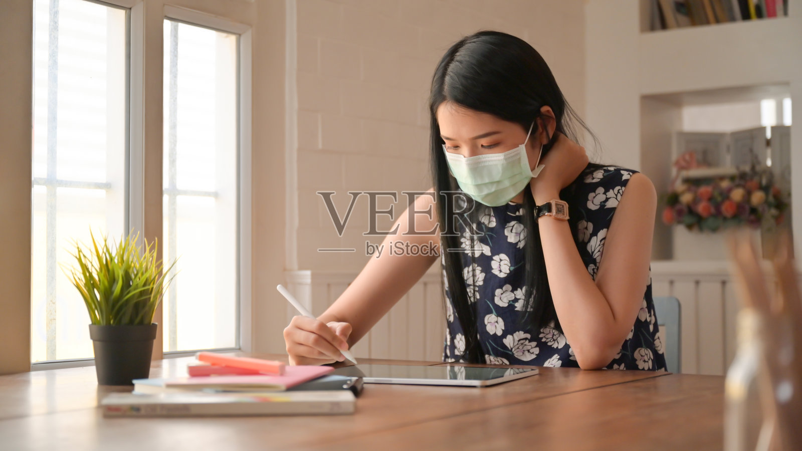 一个戴着面具坐着工作的女孩。她在家里工作以抵御Covid-19病毒。照片摄影图片