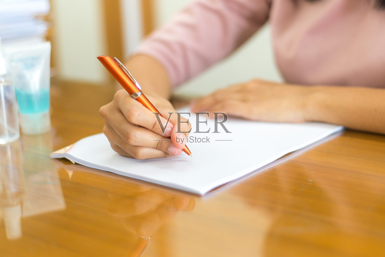 人们在家里的办公桌前写书。用手拿着纸上的橙色笔照片摄影图片