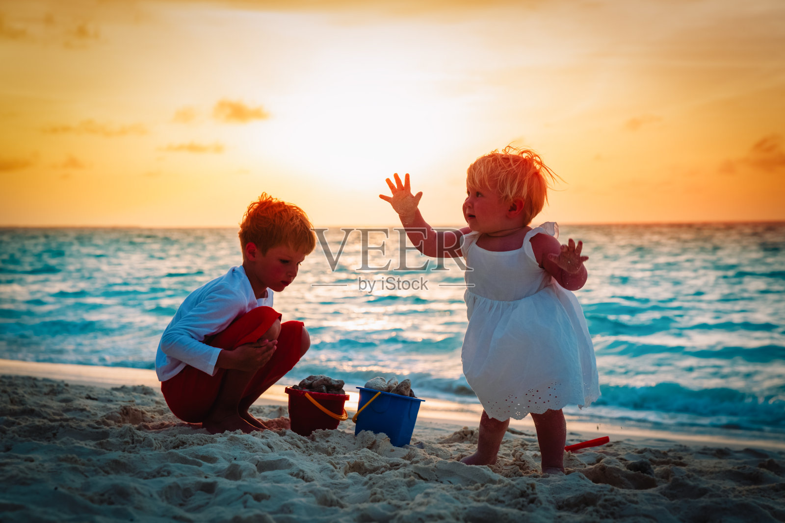 日落时分，小男孩和小女孩在海滩上玩沙子照片摄影图片