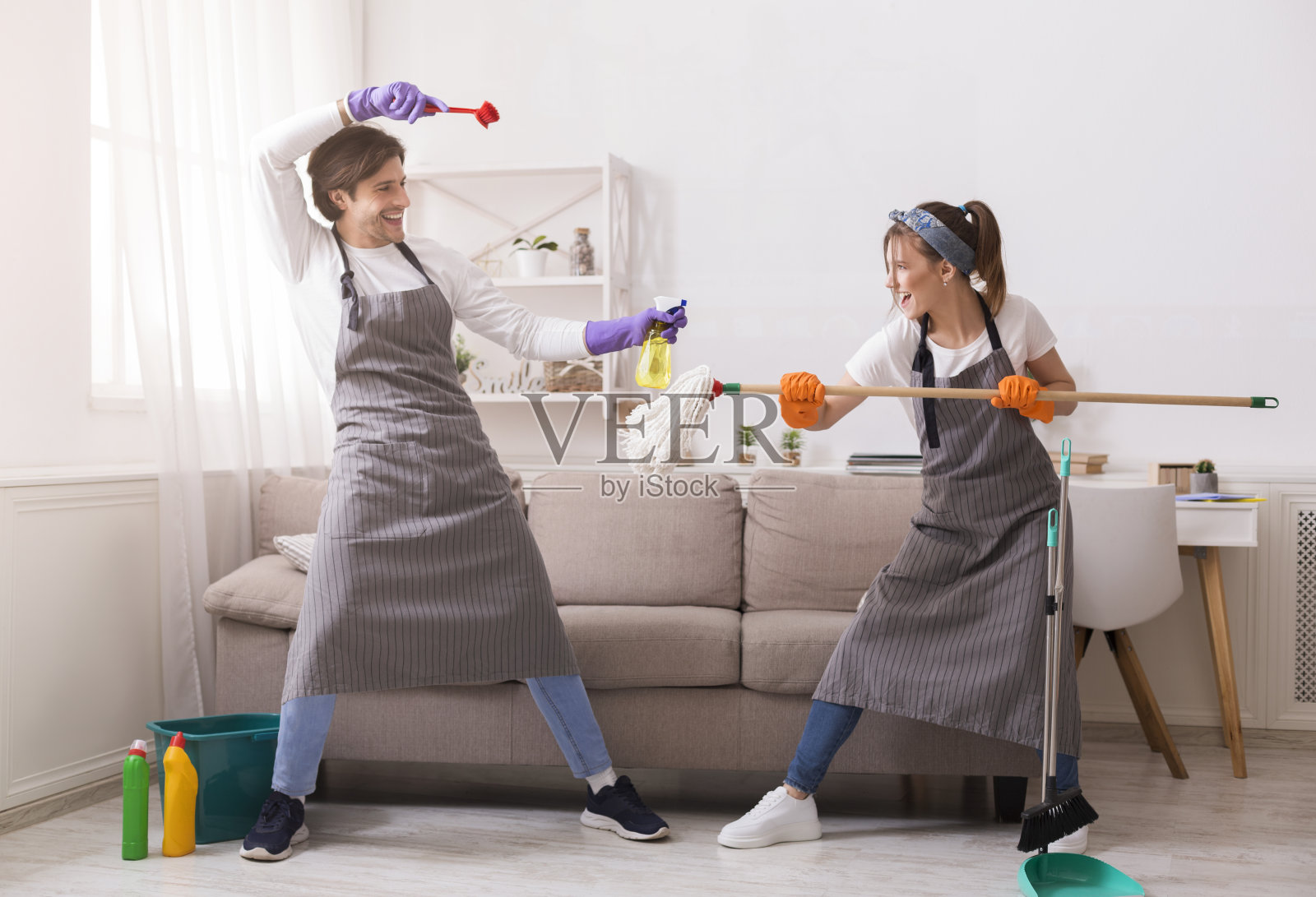 快乐的夫妇在打扫他们的公寓时，开玩笑地打架照片摄影图片