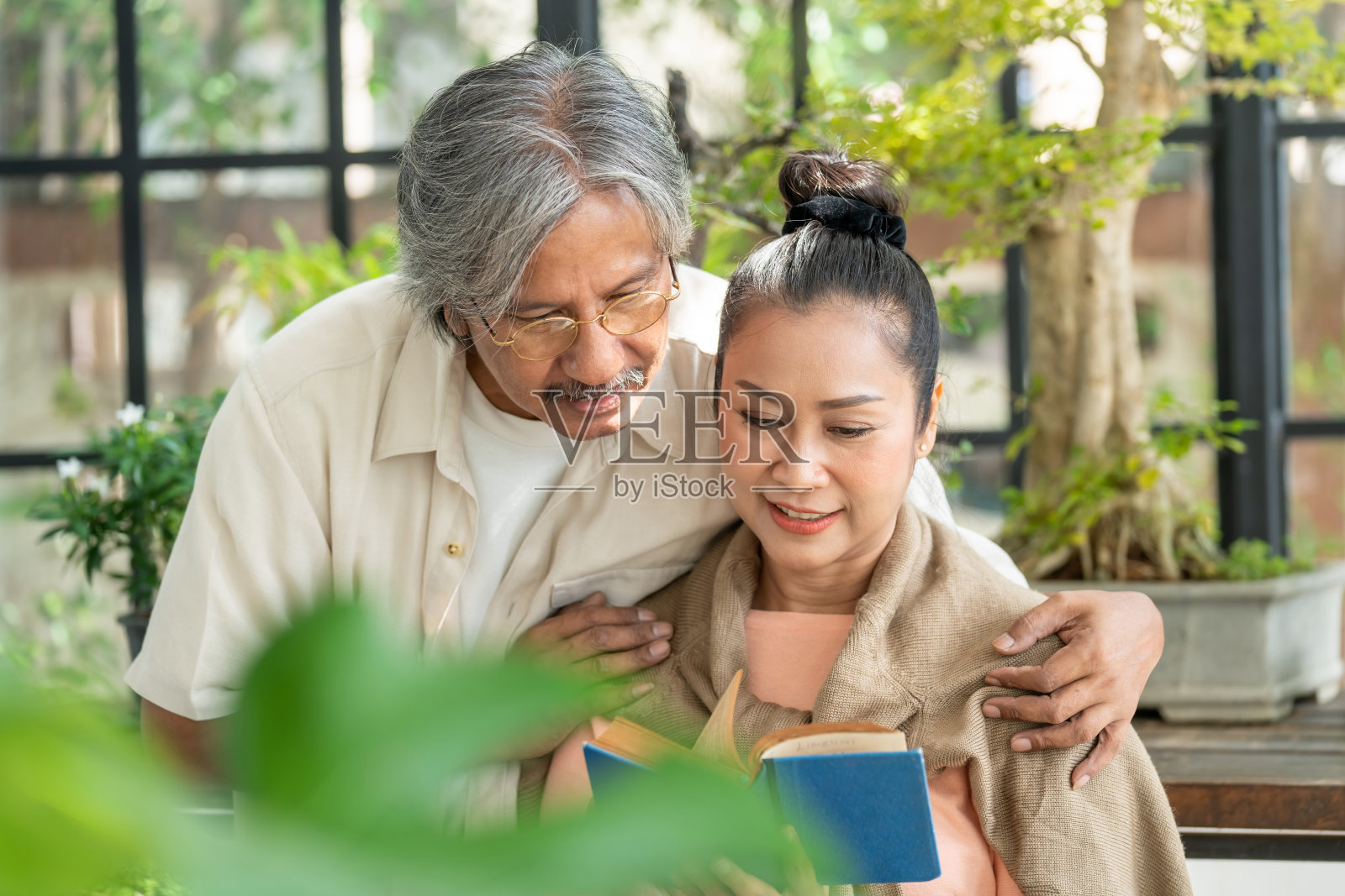 放松的亚洲老年夫妇男女在家里的温室花园里一起看书。退休老年家庭有浪漫时刻。老年人的生活方式和保健理念。照片摄影图片