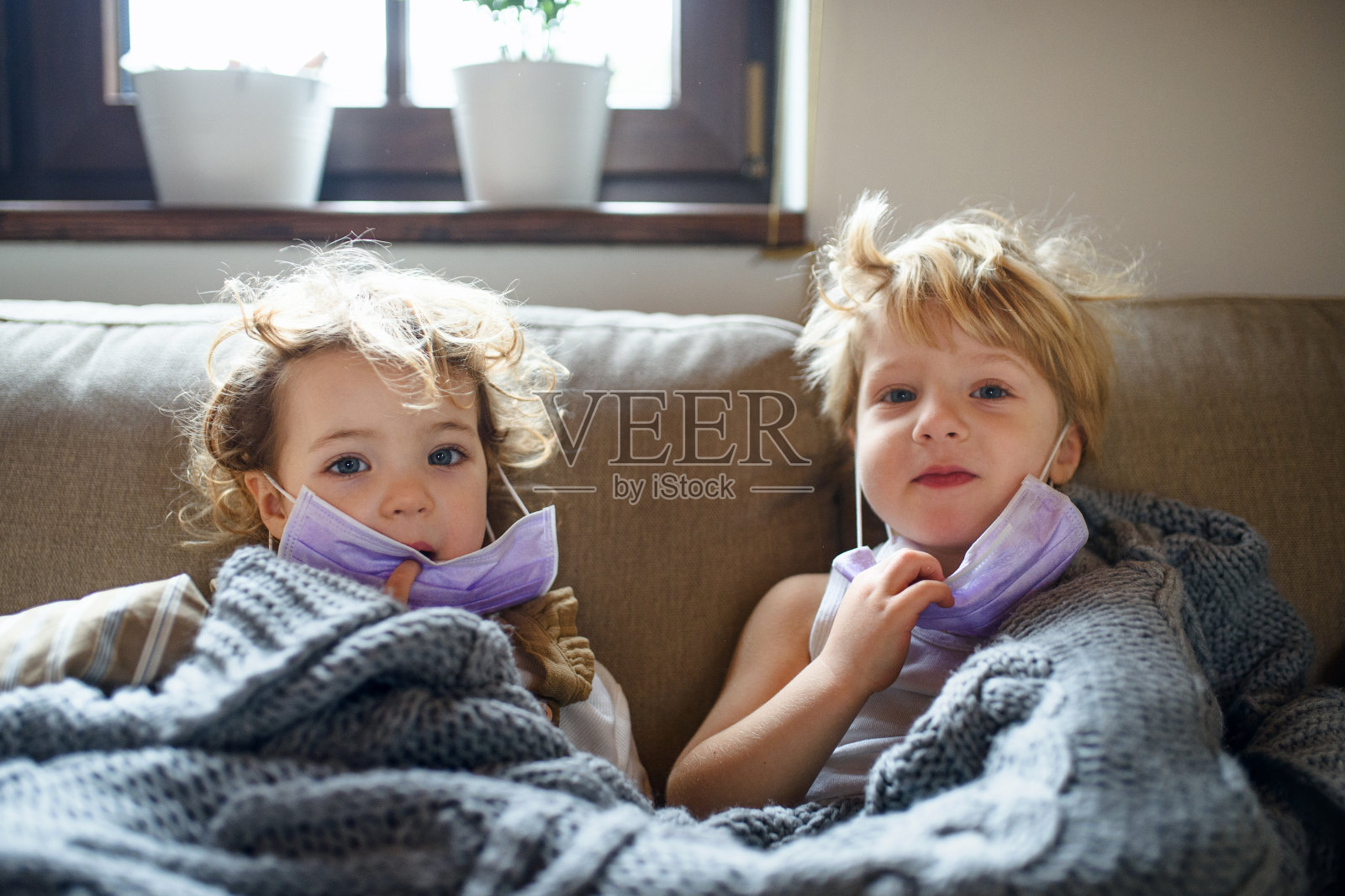 两个生病的小孩戴着口罩躺在家里的床上。照片摄影图片