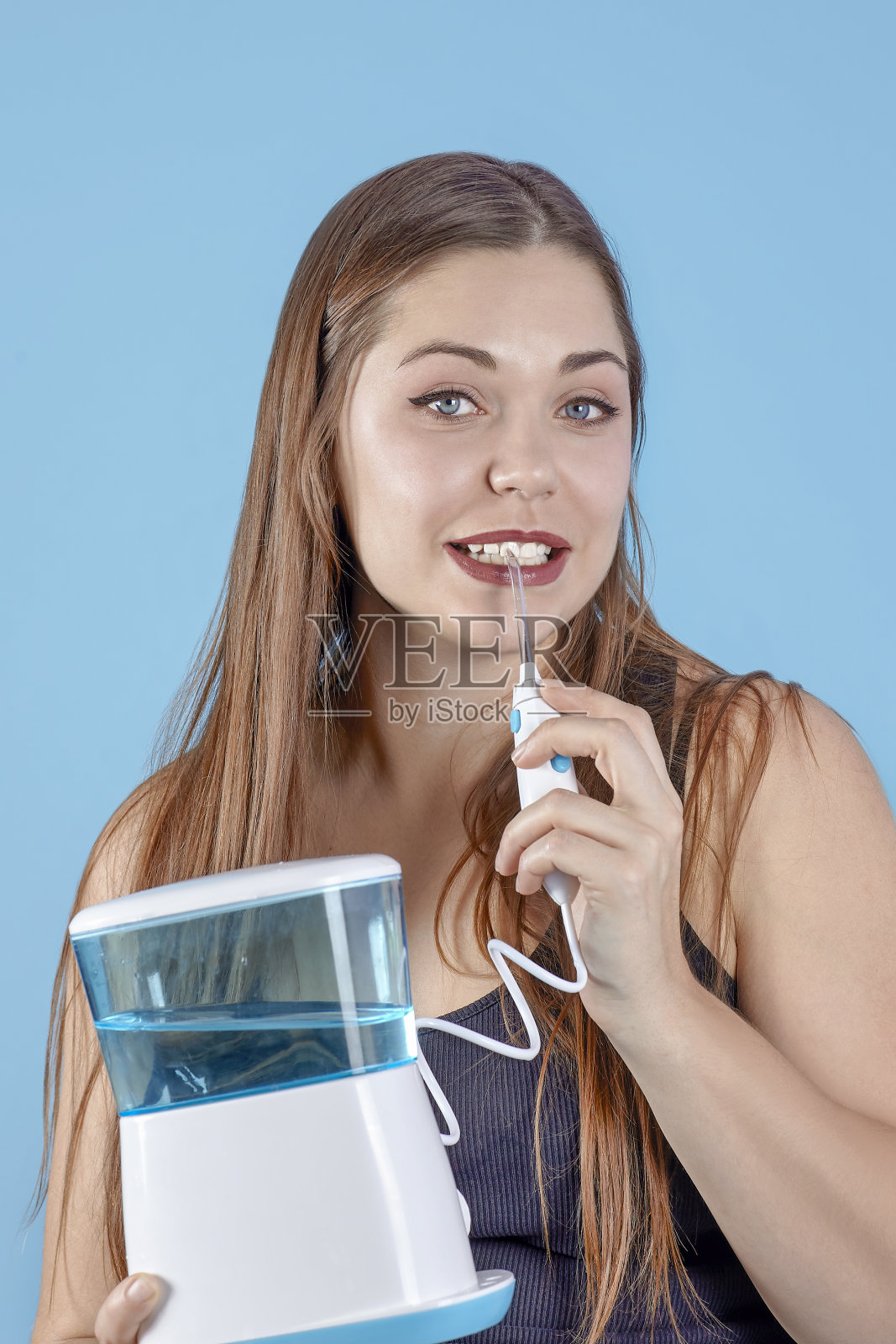 年轻美丽的女人拿着口腔冲洗器，微笑着露出洁白的牙齿。照片摄影图片