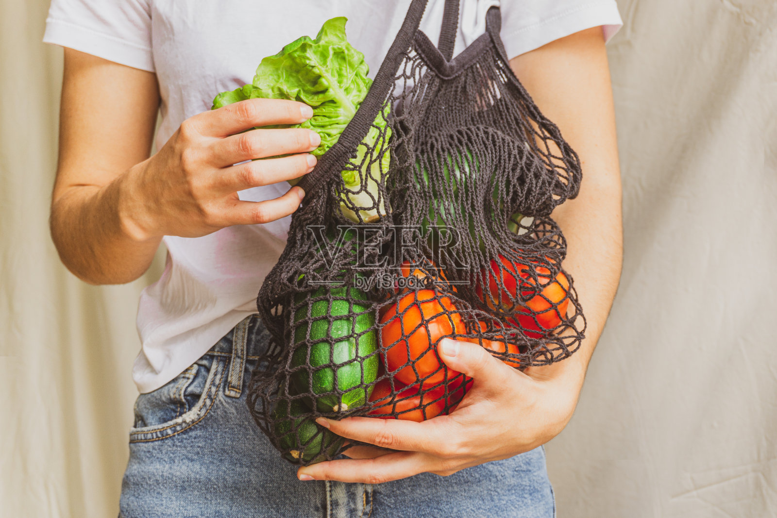 女孩拿着装满蔬菜的网状购物袋，从里面取出来自农场的新鲜生菜。可持续、零浪费、无塑料的生活方式。拯救地球的概念照片摄影图片