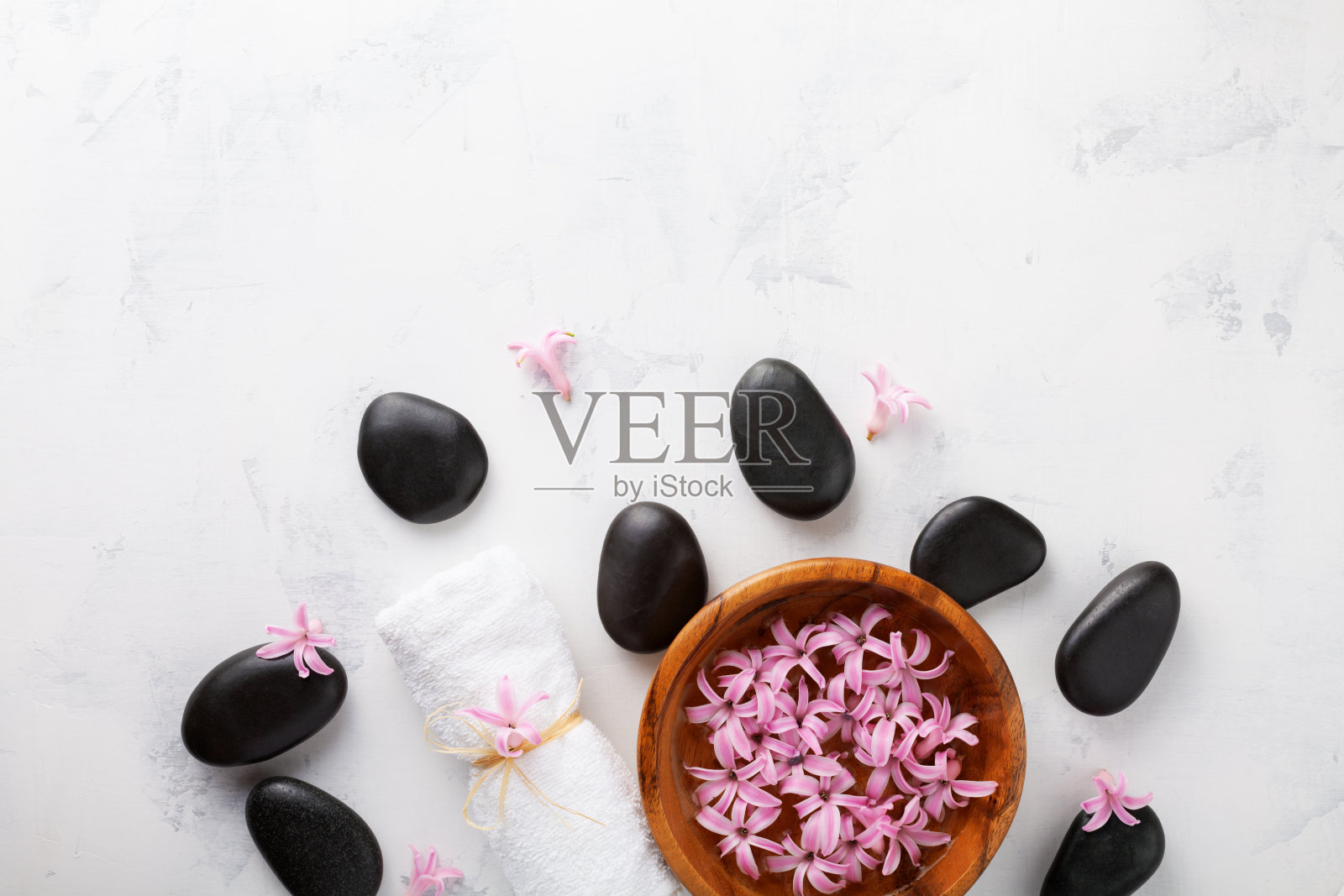 美容，水疗中心背景与黑色按摩石和鲜花在碗上的白色桌子顶视图。放松和健康的概念。平的。照片摄影图片