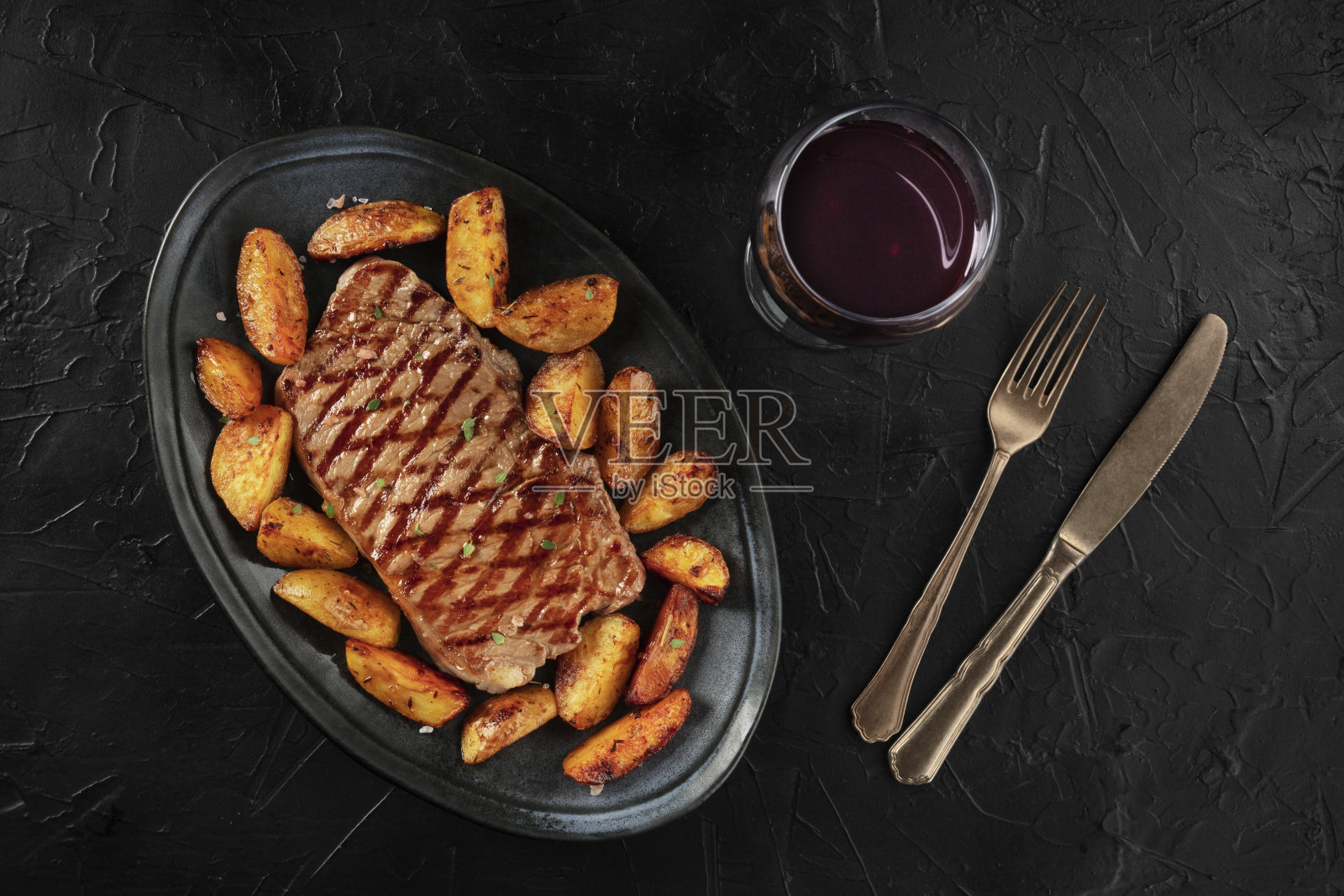 烤牛排和烤土豆角，一杯葡萄酒，从顶部拍摄的黑色背景照片摄影图片