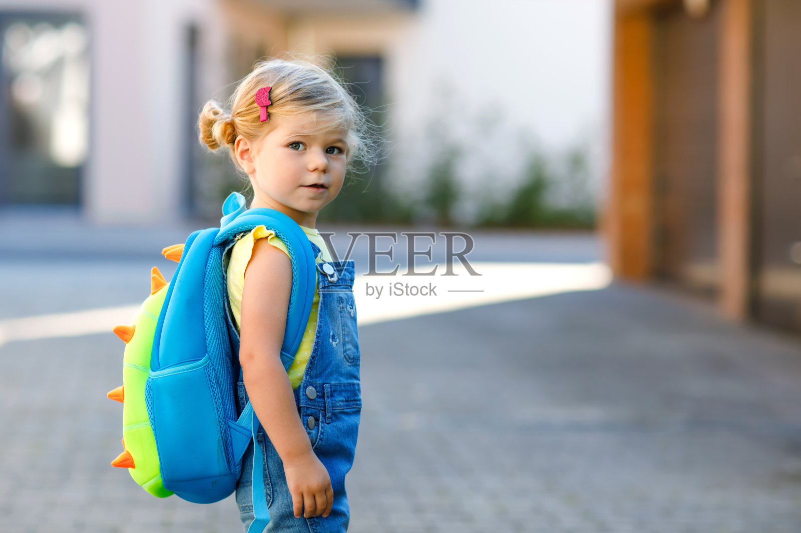 可爱的蹒跚学步的小女孩第一天去幼儿园。健康美丽的宝宝步行去幼儿园和幼儿园。快乐的孩子背着背包在城市的大街上，在户外。照片摄影图片