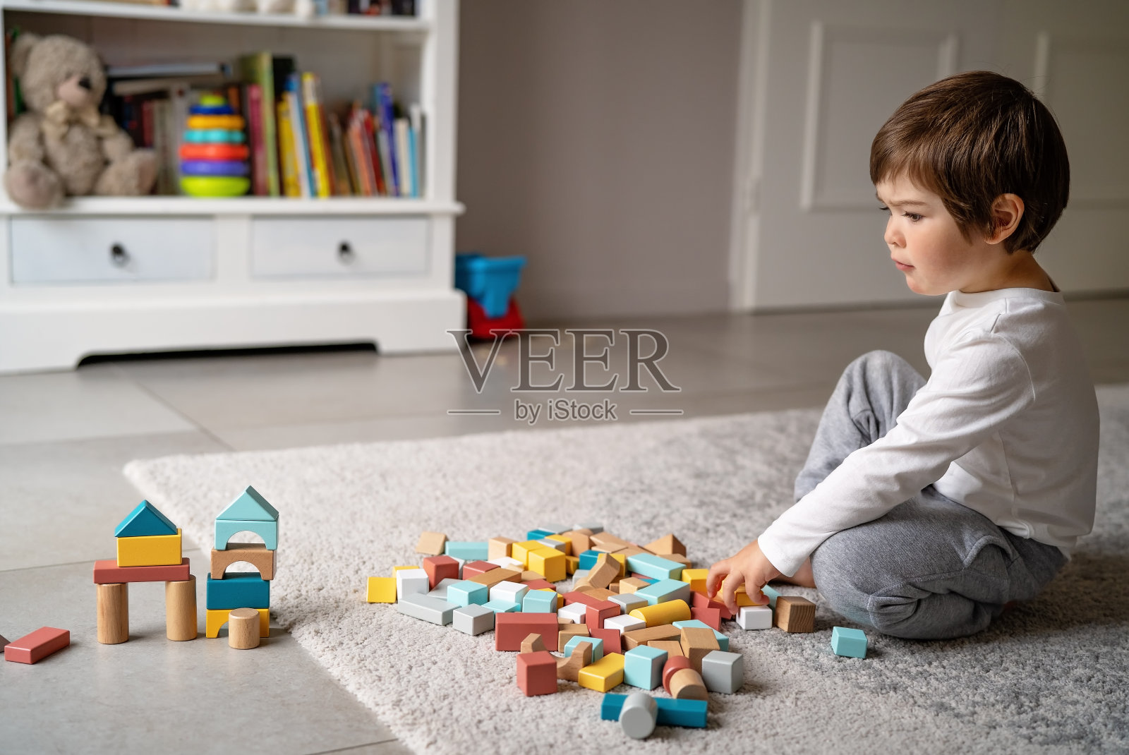 一个蹒跚学步的小男孩在隔离期间独自在家玩彩色积木。儿童运动技能、创造力和想象力发展游戏。照片摄影图片