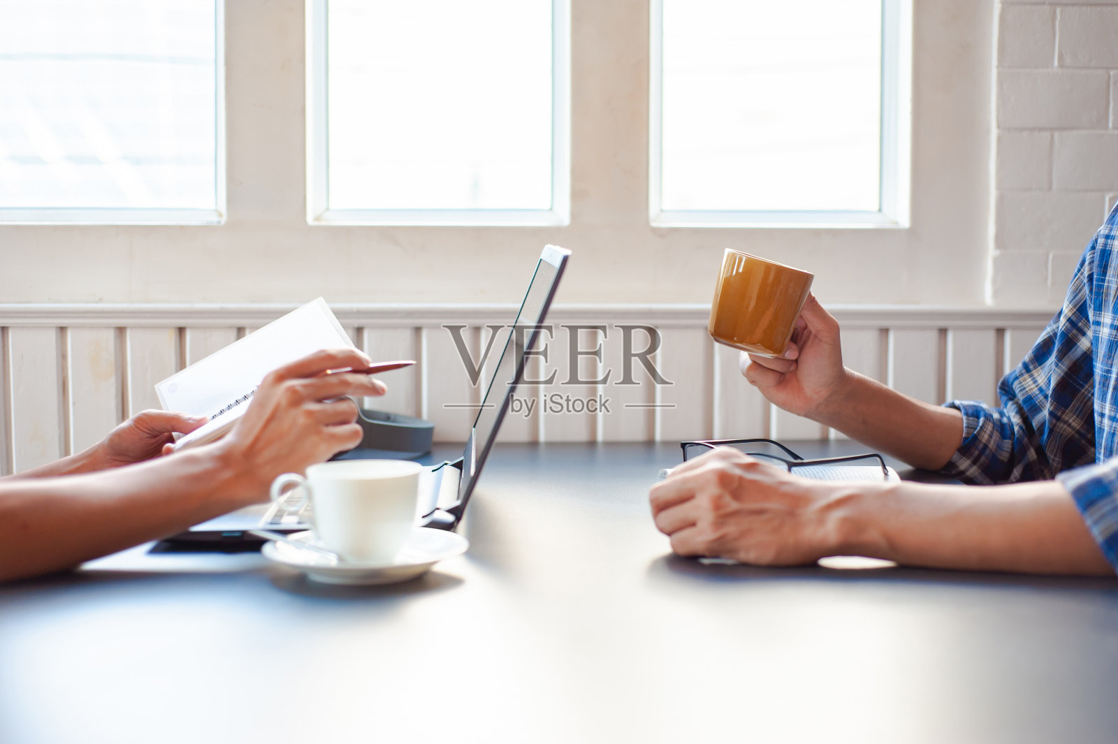 一个年轻人一边用笔记本电脑工作一边喝咖啡和同事聊天。照片摄影图片
