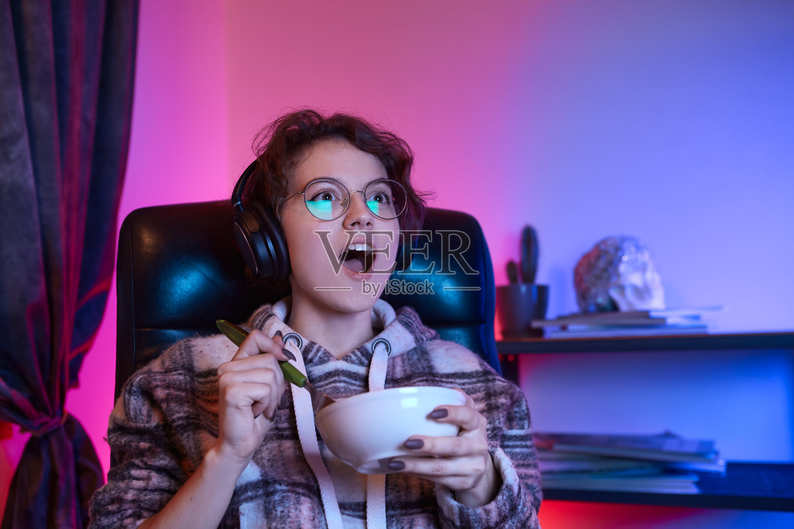 兴奋的年轻女子在电脑上看视频，吃零食。背景是霓虹灯。照片摄影图片