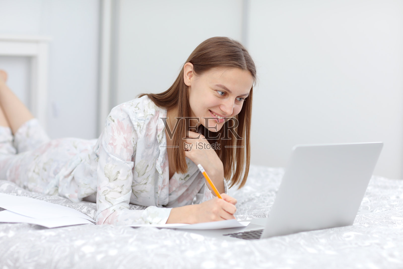 美丽的年轻女人从家里工作-女企业家在床上与笔记本电脑，文书工作从家里。快乐的女孩看着笔记本做笔记。隔离。冠状病毒照片摄影图片