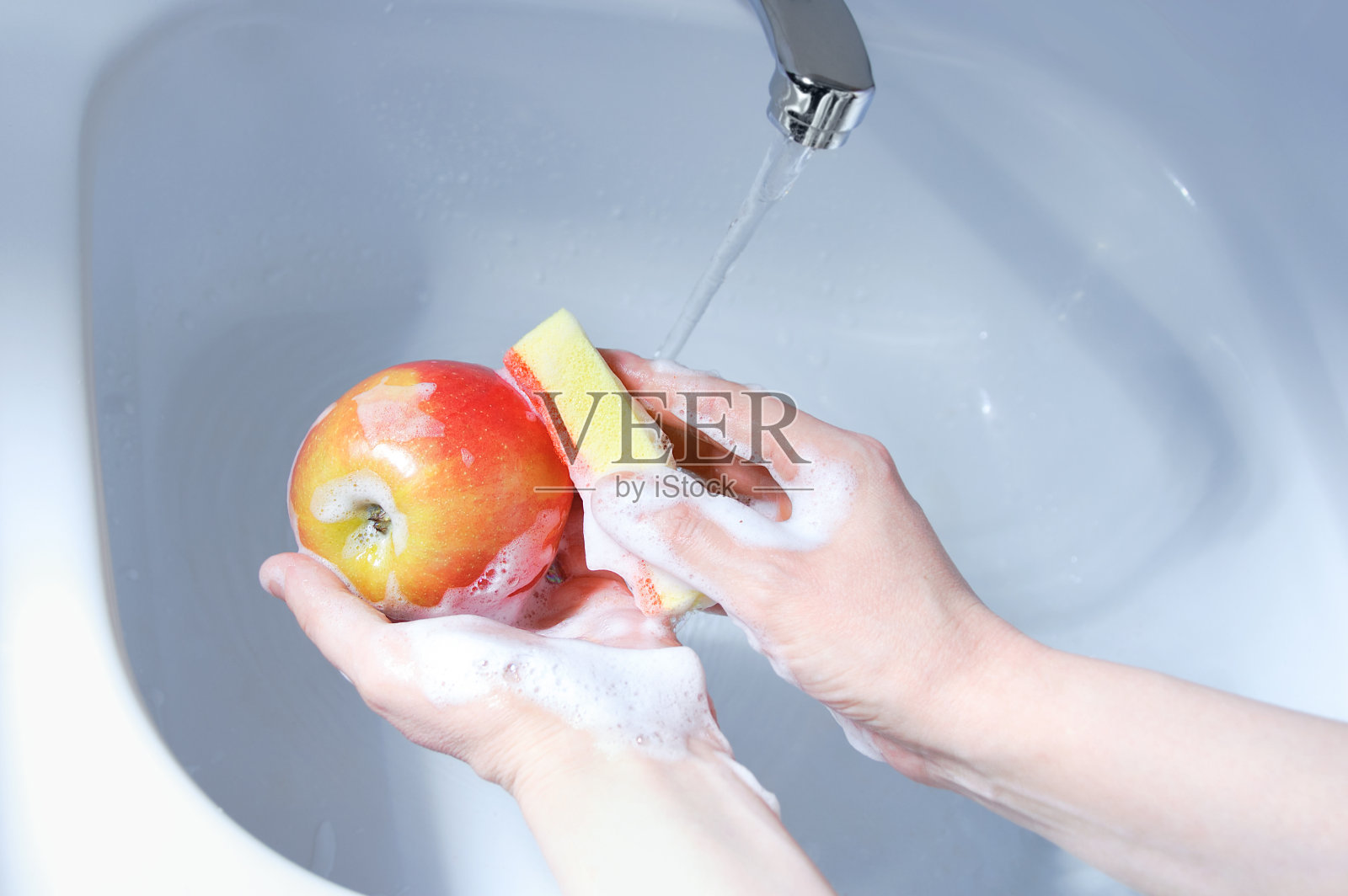 在脸盆里用海绵蘸肥皂泡沫洗苹果。从以上观点。照片摄影图片