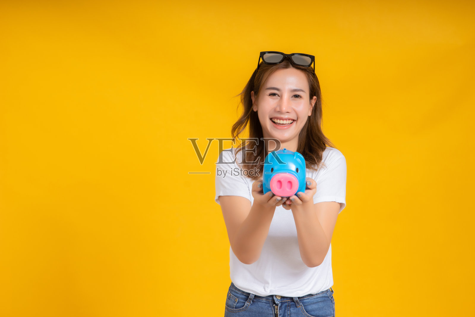 肖像快乐的年轻亚洲妇女抱着存钱罐为未来和业务收入收入积极情绪在白色t恤，黄色背景孤立的工作室拍摄和复制空间。照片摄影图片