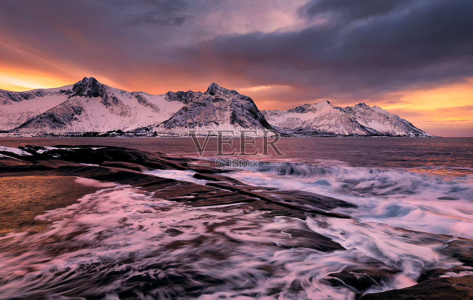 在一个黑暗的多云的日子，Tungeneset角，Senja，挪威，从五颜六色的岩石日落和岩石池到雪山俯瞰Ersfjord。欧洲。长时间曝光照片摄影图片